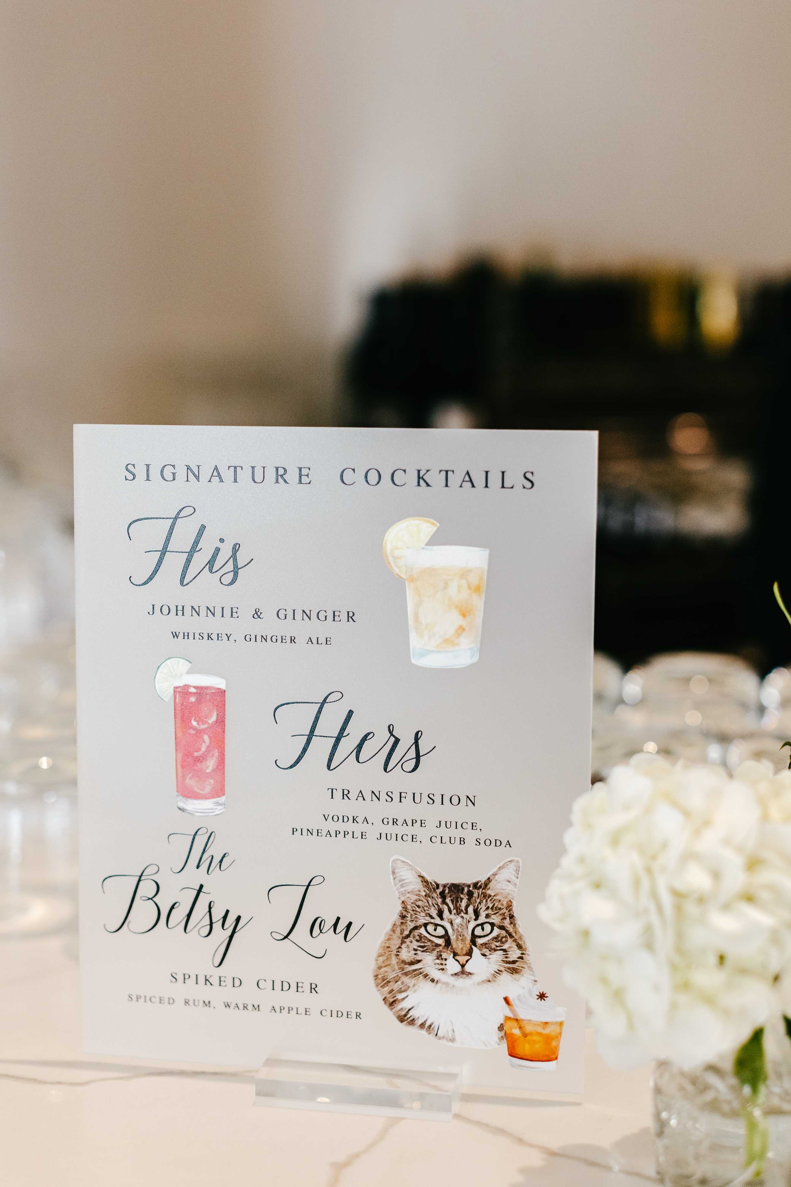 A custom signature cocktail menu sign featuring His and Hers drinks with a personalized cat illustration, displayed elegantly for a wedding reception.