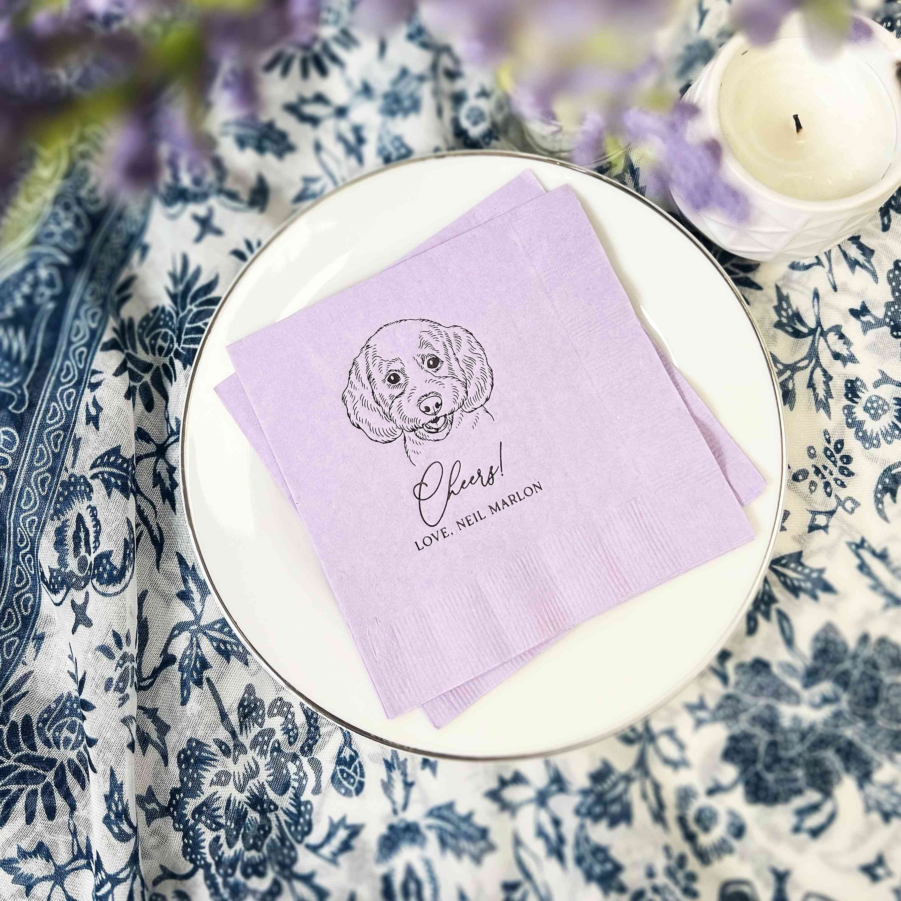 Personalized lilac paper napkins featuring a custom dog illustration and Cheers text, ideal for a wedding or celebration.