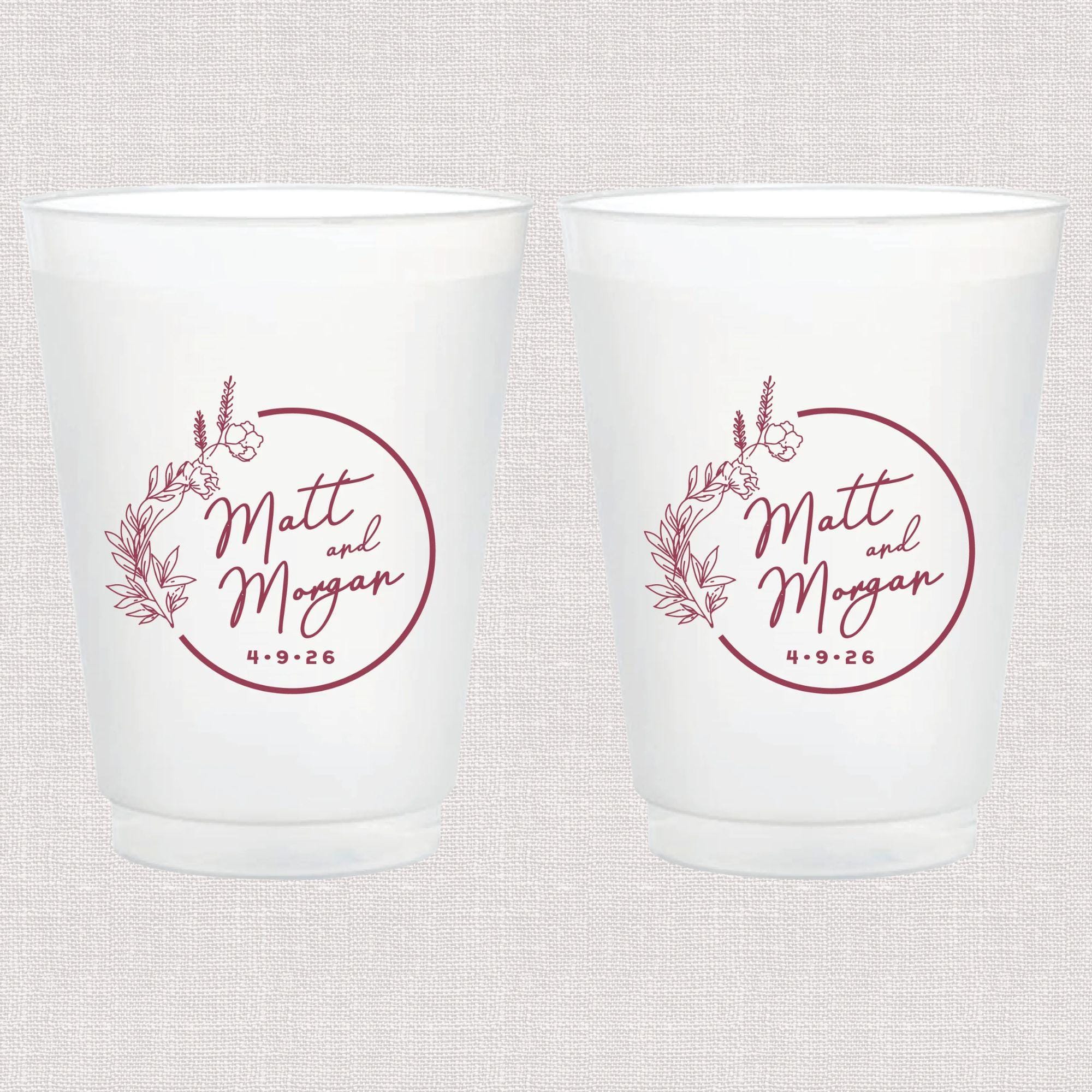 Two frosted white cups with mauve floral wreath design and personalized names "Matt and Morgan" with wedding date.