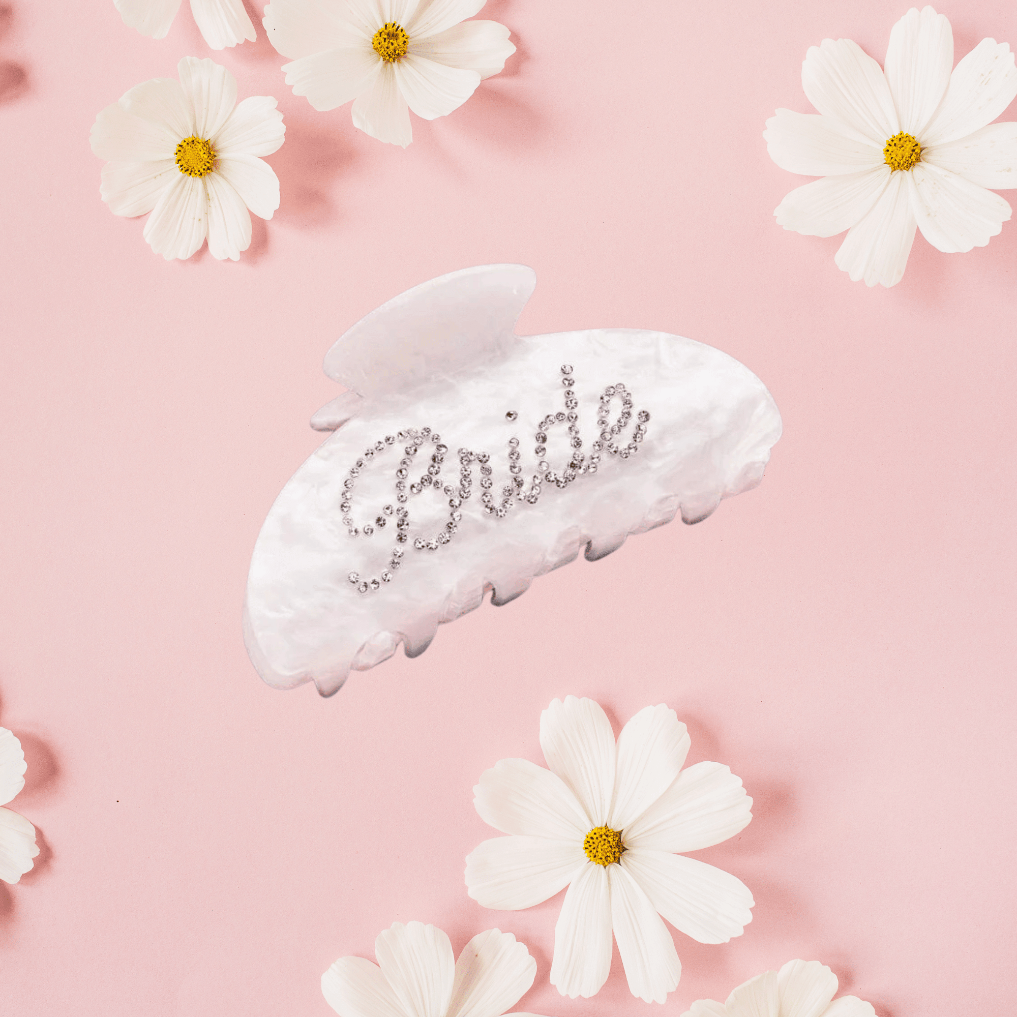 White pearlescent claw clip with "Bride" in sparkly silver text, surrounded by white daisies on pink background.