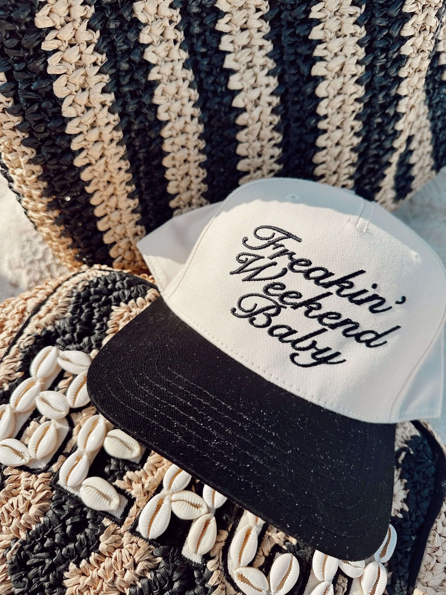 Black and cream trucker hat with "Freakin' Weekend Baby" text on white front panel, displayed on textured striped blanket.