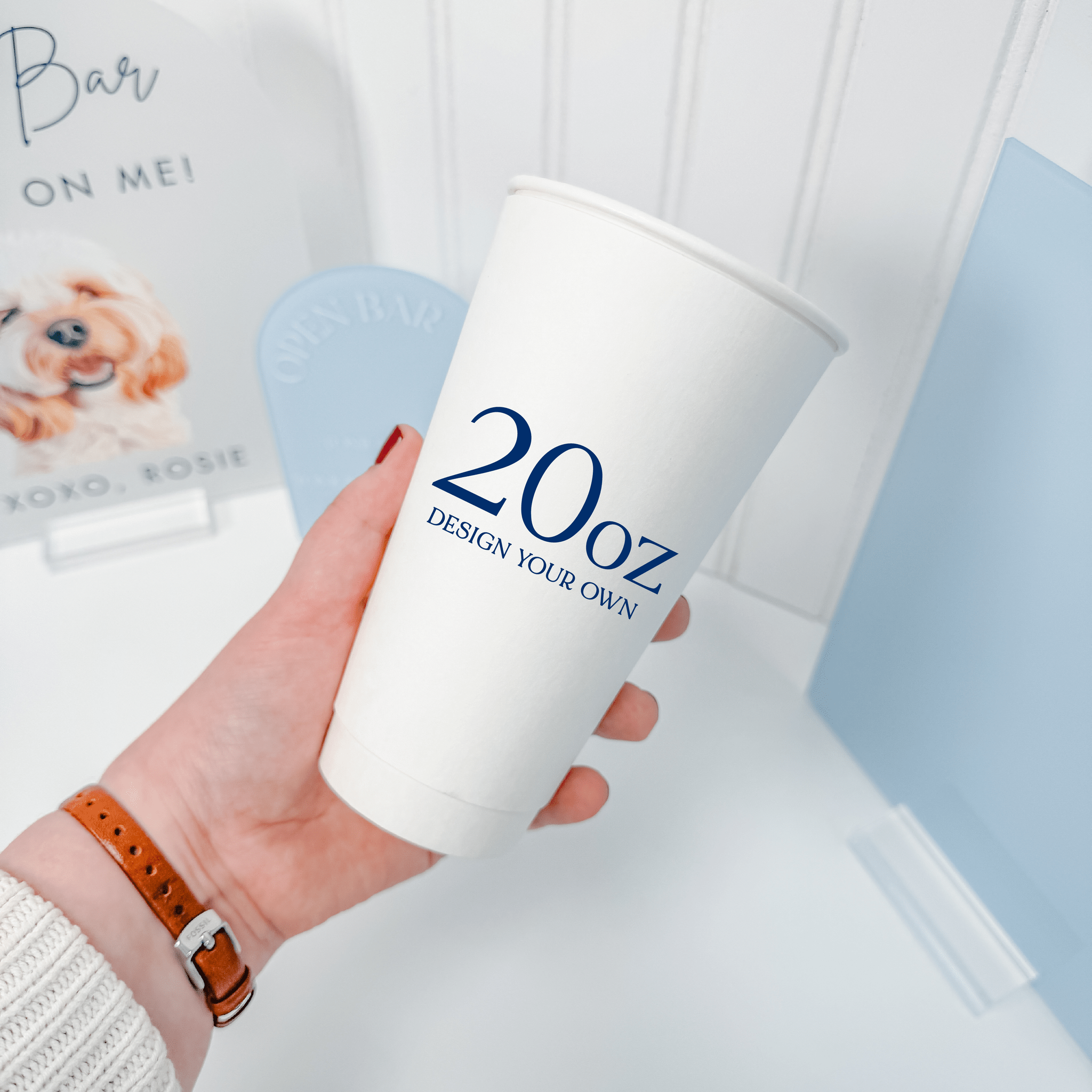 Hand holding a 20 oz white paper cup with a personalized custom design in navy