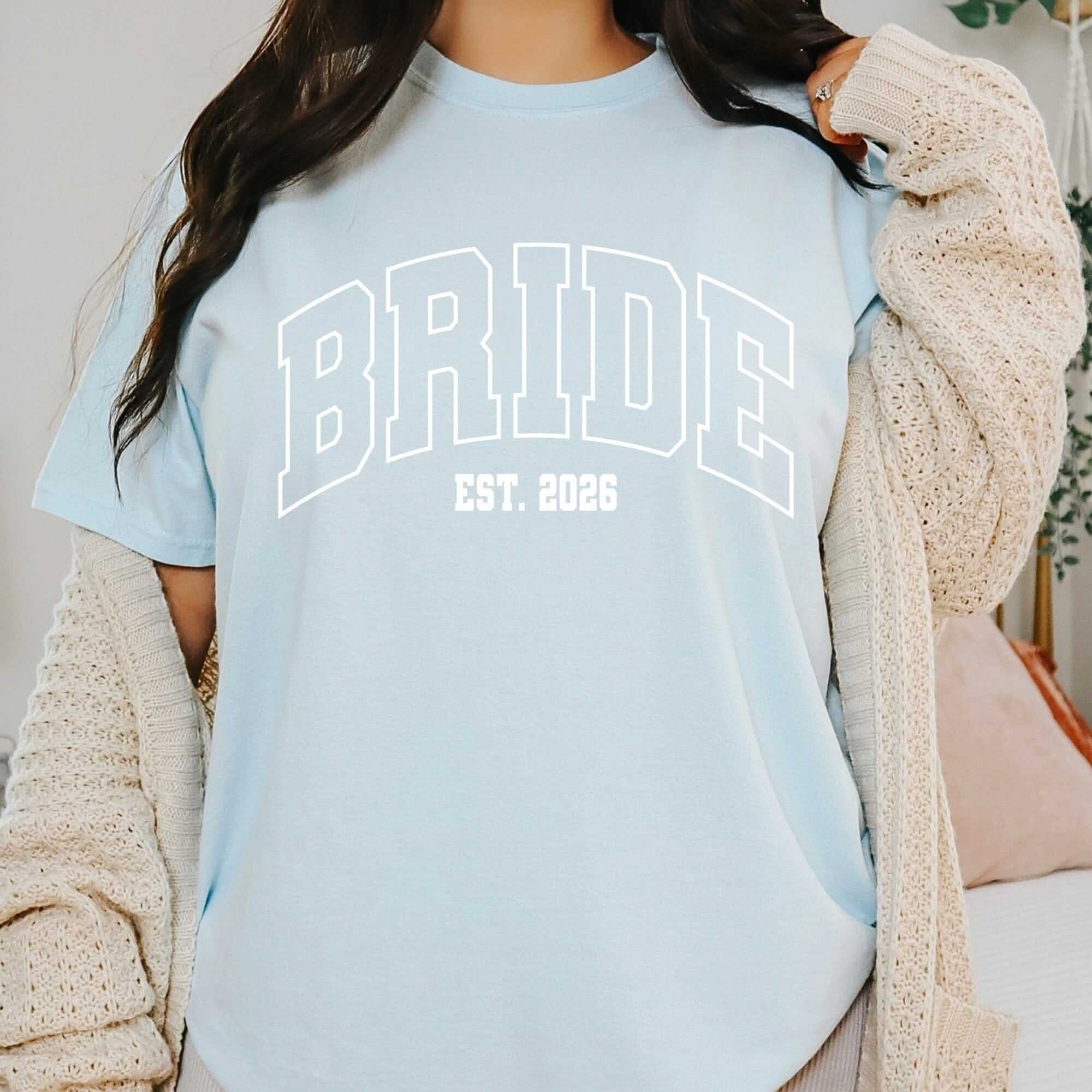 A light blue short-sleeved bridal t-shirt, made of soft fabric, featuring a collegiate-style graphic design, ideal for pre-wedding events or casual wear.
