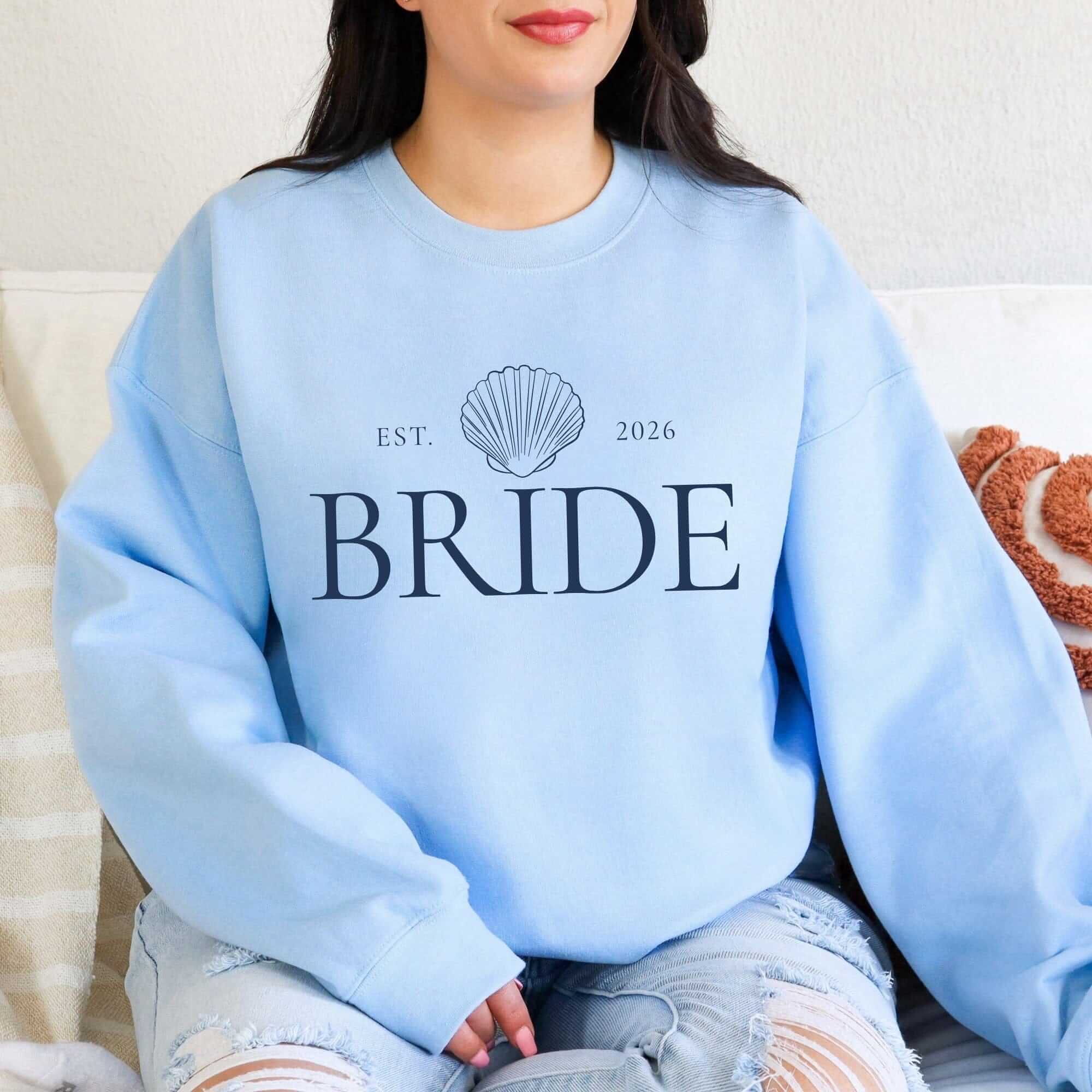 A light blue crewneck sweatshirt made from soft fabric, featuring a seashell graphic, ideal for bridal events.