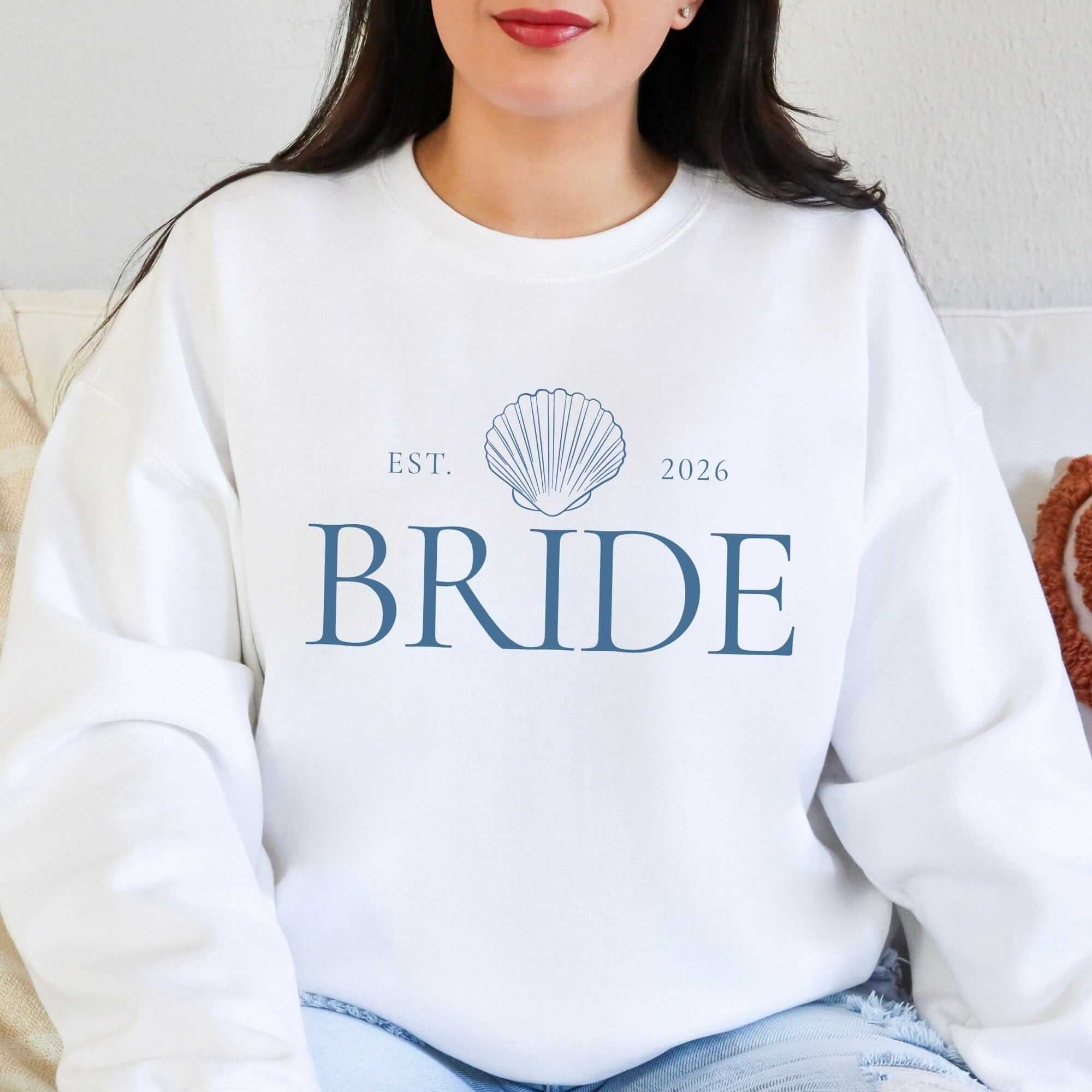 A white crewneck sweatshirt features a blue seashell graphic, ideal for a wedding or bridal event.