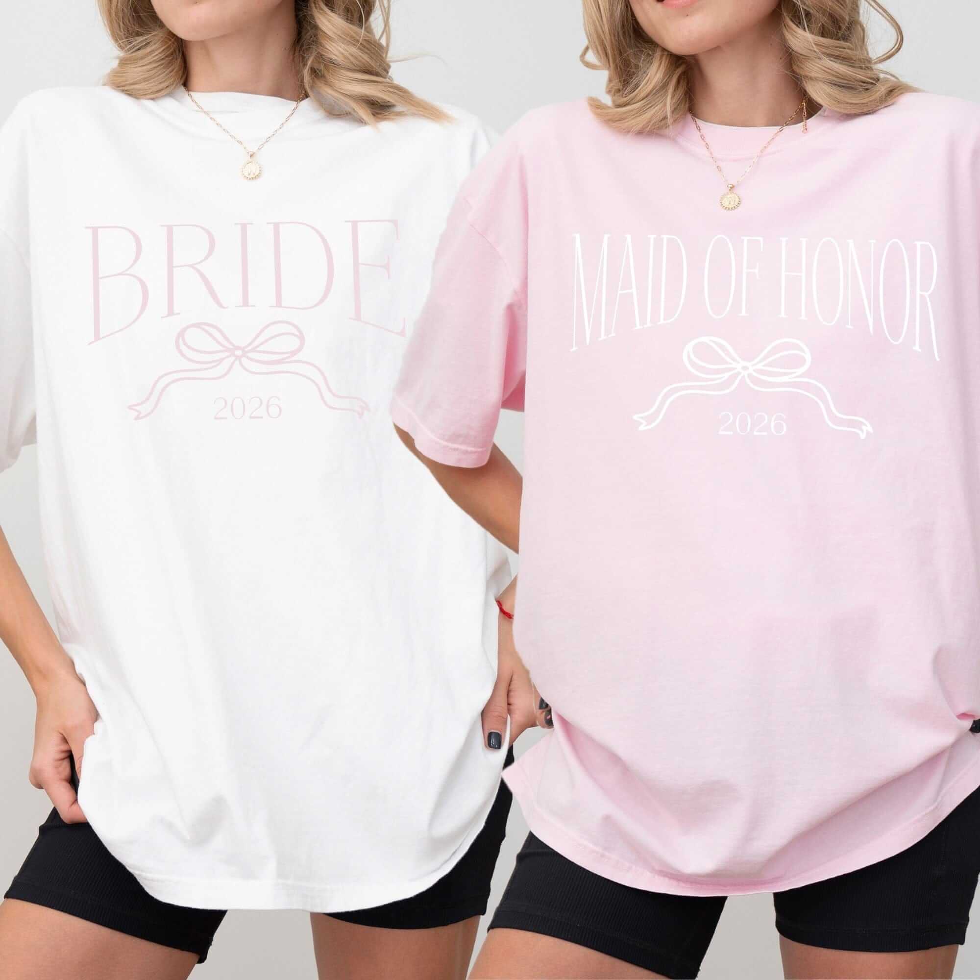 Two women model personalized oversized cotton t-shirts for a wedding celebration, one white with light pink graphics and another light pink with white graphics, both featuring a decorative bow design.