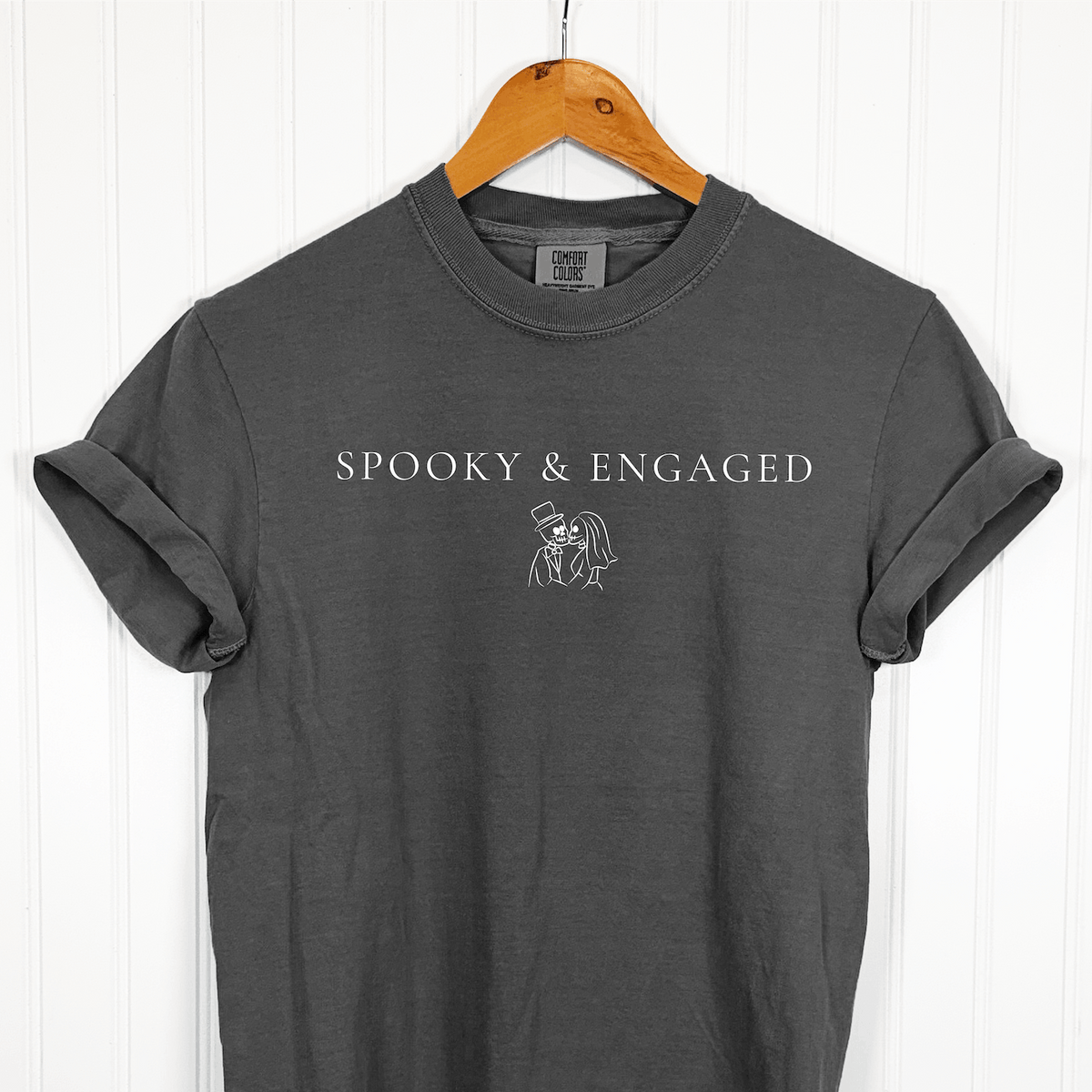 Charcoal gray Comfort Colors Halloween bride t-shirt with Spooky & Engaged lettering and skeleton couple design, displayed on a wooden hanger.