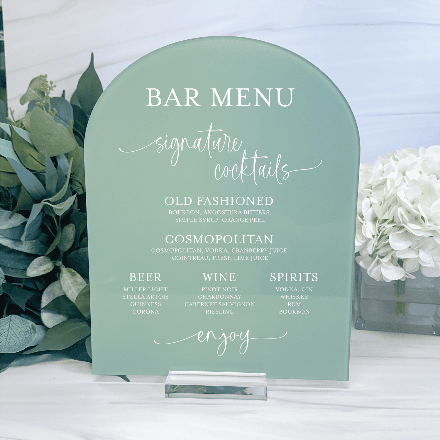 Sage green arch-shaped acrylic bar menu sign with white text listing signature cocktails, beer, wine, and spirits options for a wedding event.