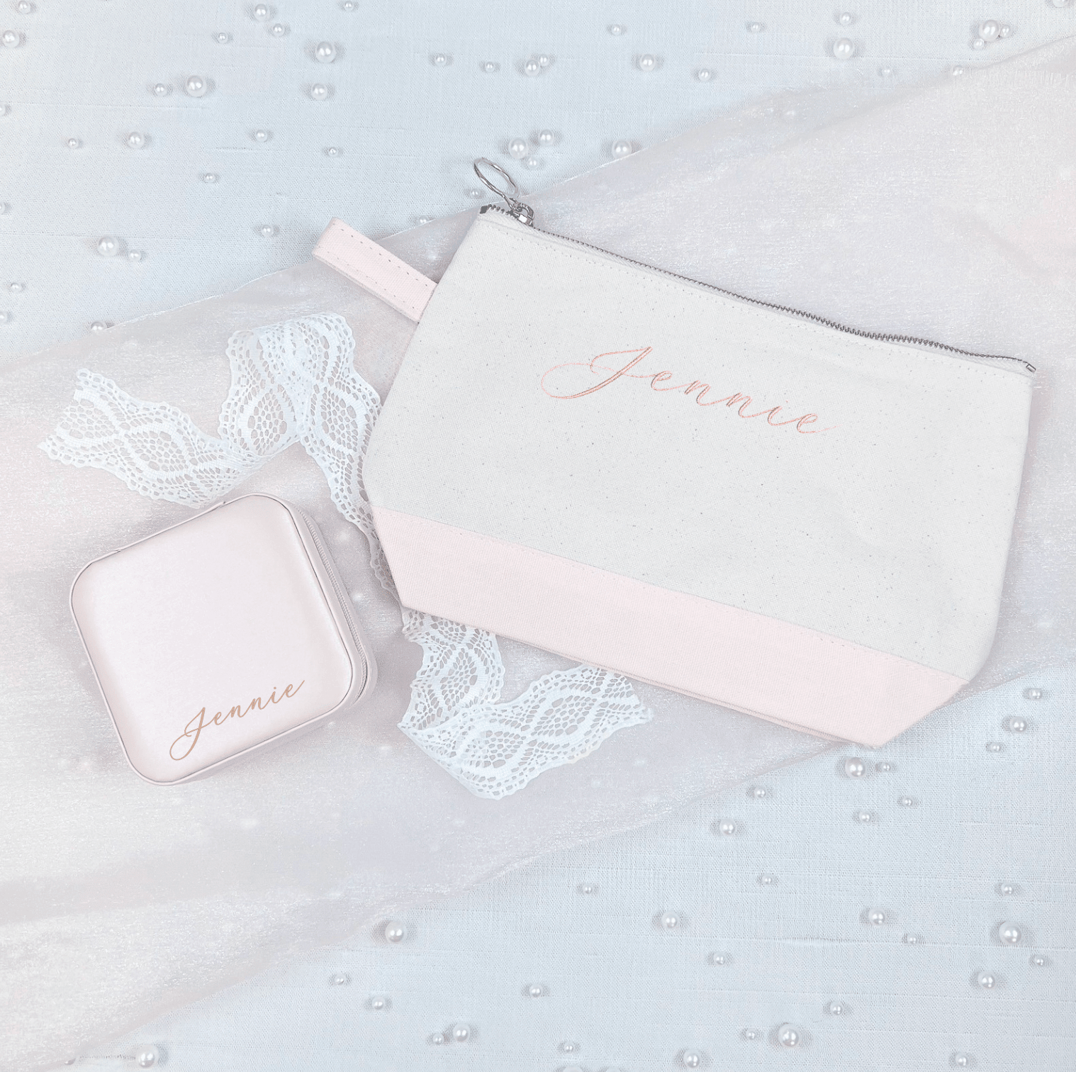 Blush pink cosmetic bag and jewelry case set with "Jenee" personalization in rose gold script, displayed on white lace fabric.