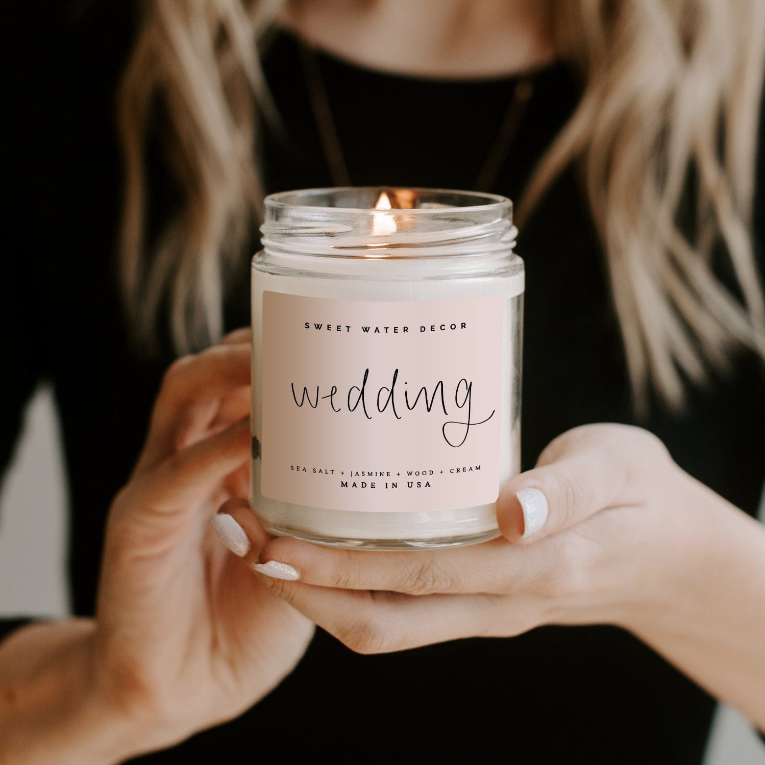 Clear soy candle jar with "wedding" text held in hands, lit flame visible, made in USA label shown