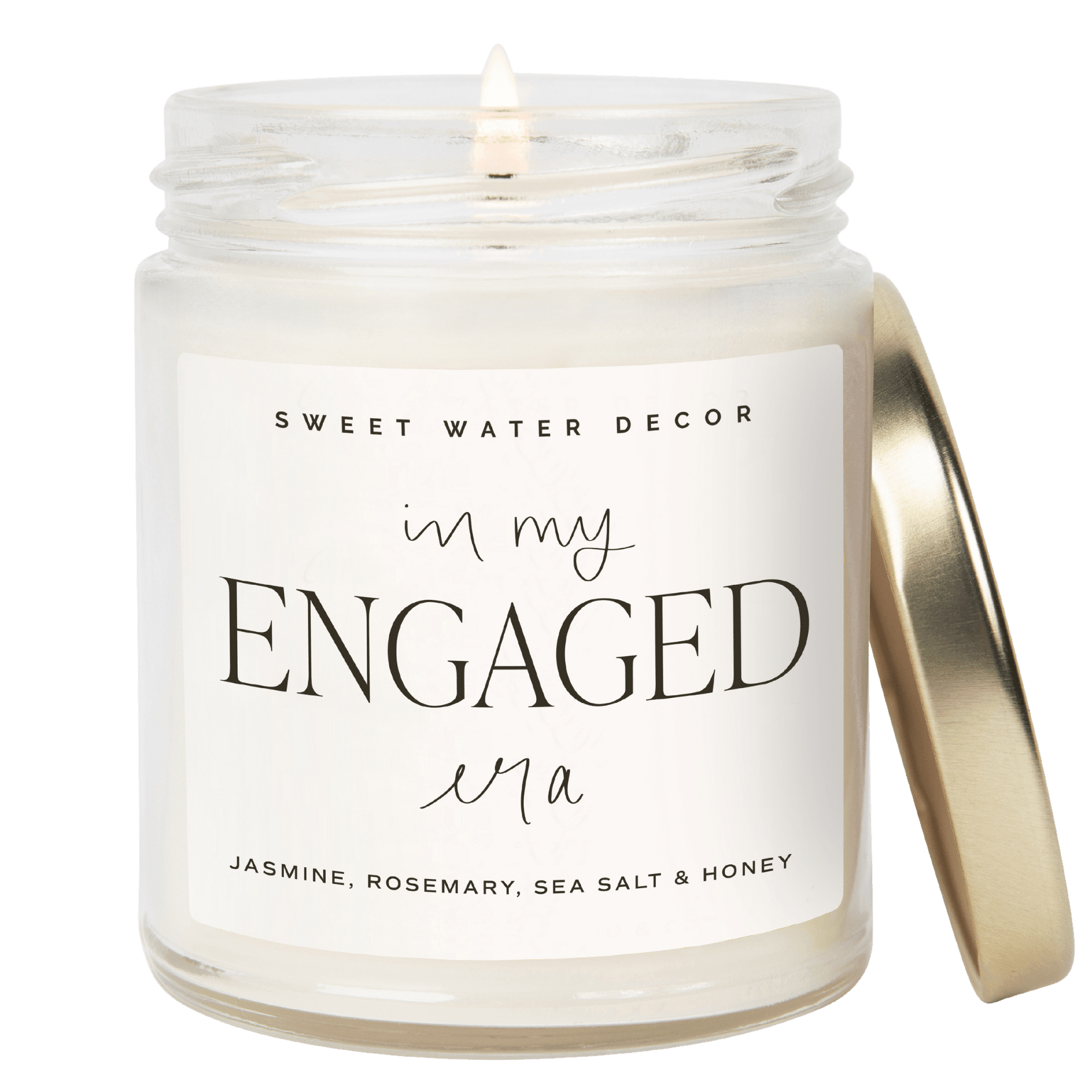 White soy candle jar with "in my ENGAGED era" text and scent notes, gold lid beside it