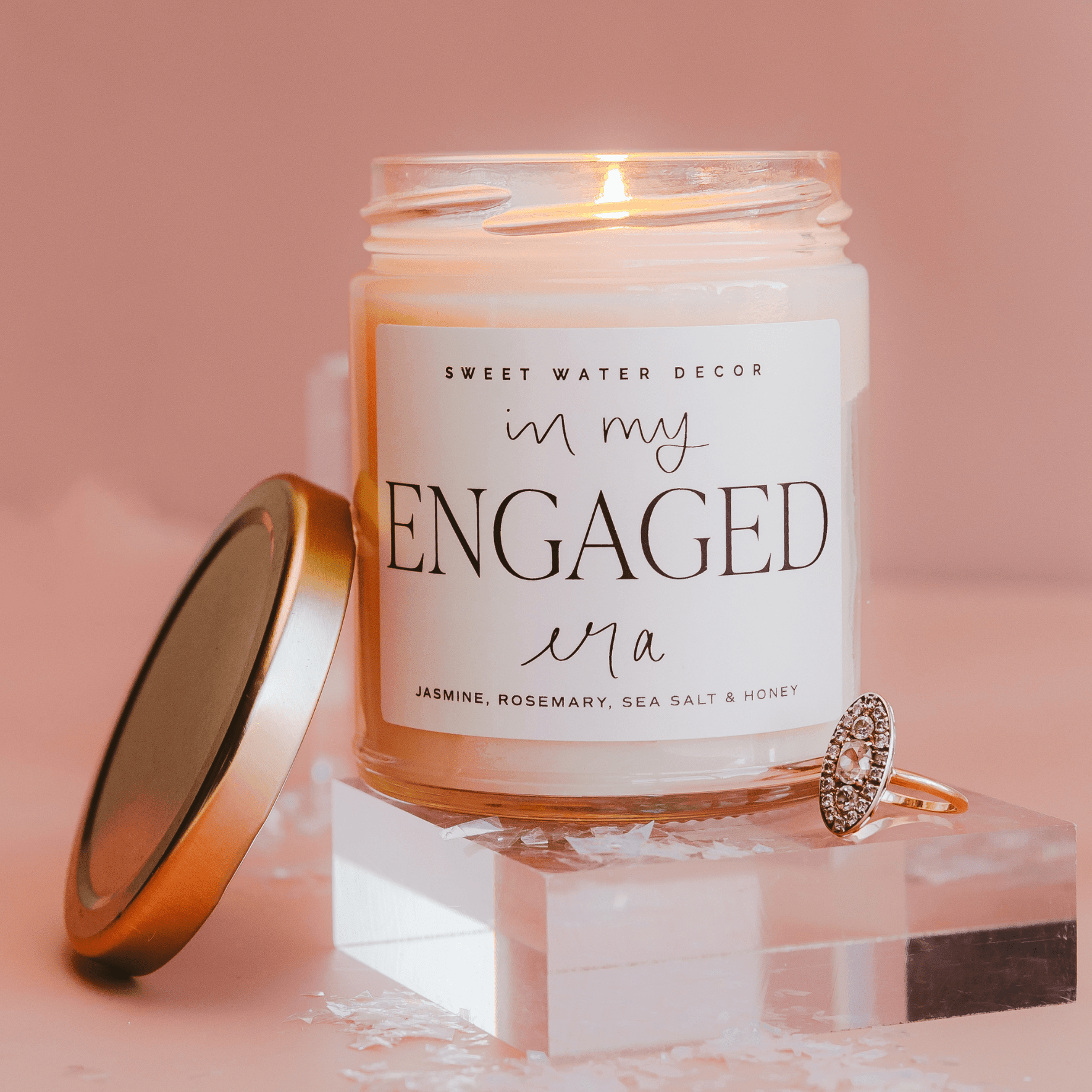 Clear glass soy candle with copper lid reading "in my ENGAGED era" in script and serif text, jasmine rosemary sea salt and honey scent.