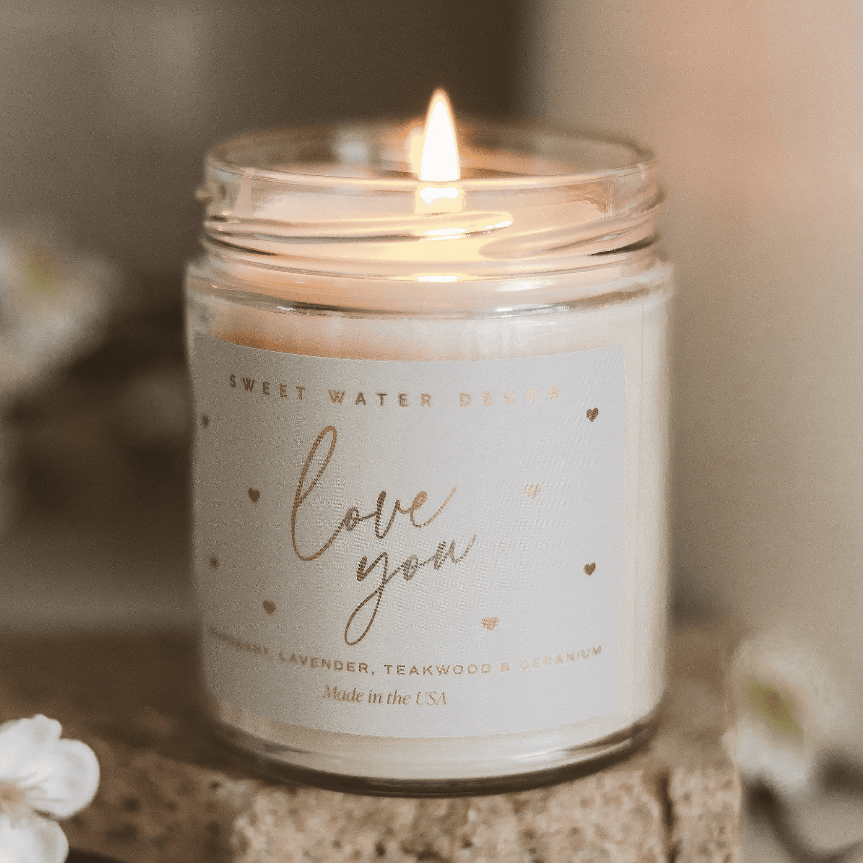 Lit soy candle in clear glass jar with "love you" text and small hearts in gold lettering on white label.