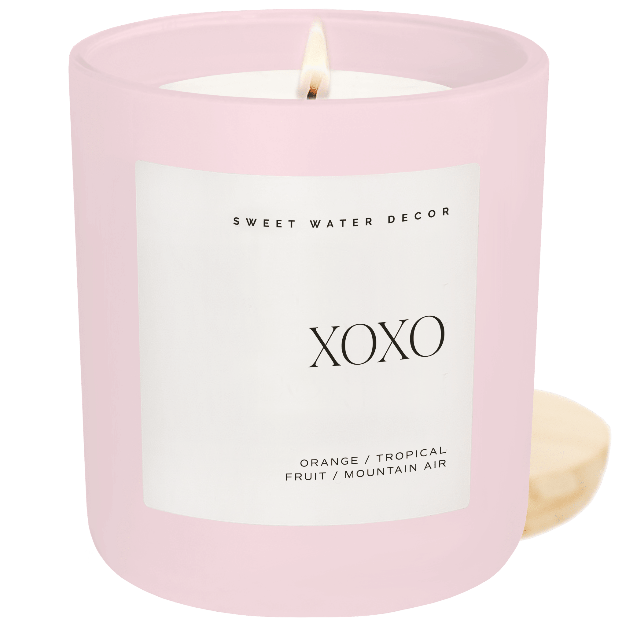 Pink matte jar candle with white label reading "XOXO" and scent notes of orange, tropical fruit, and mountain air by Sweet Water Decor