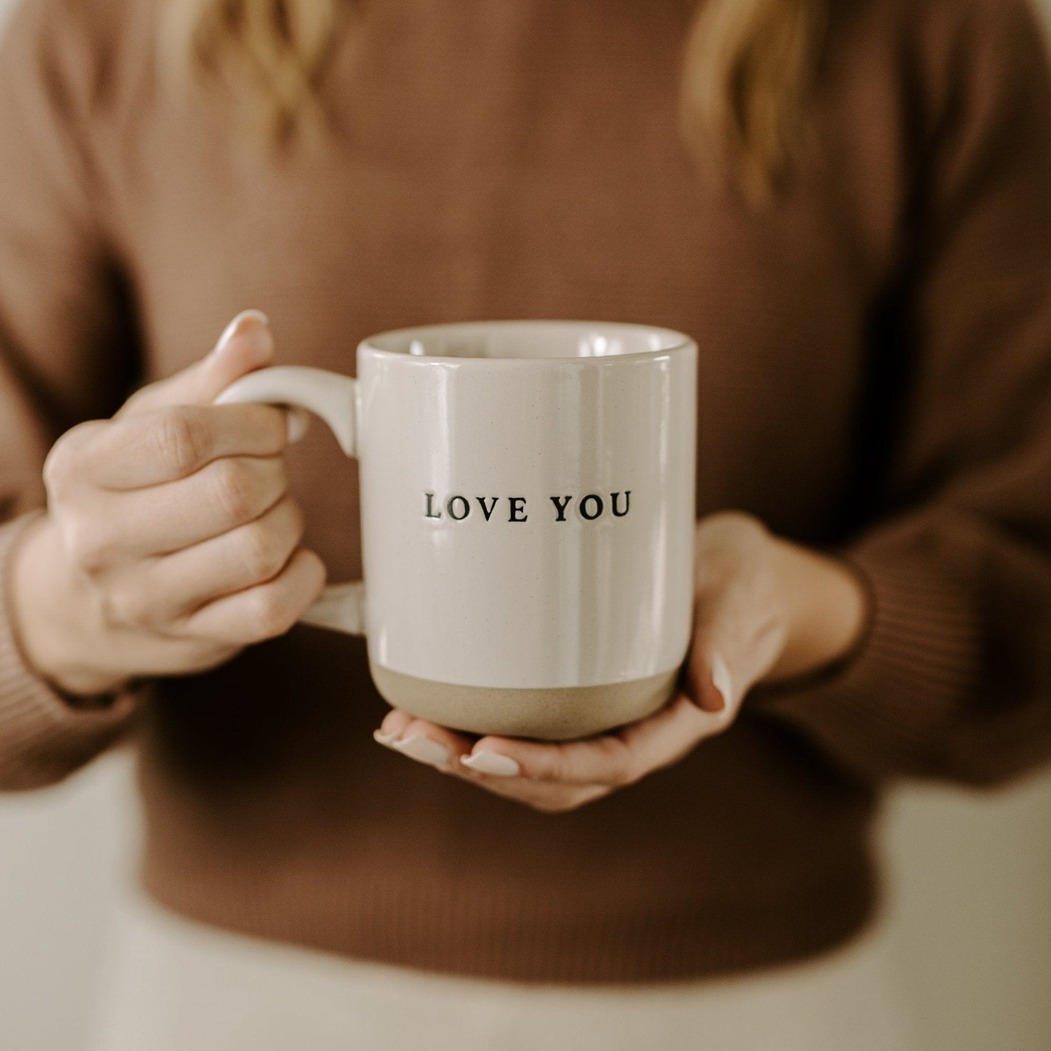 Cream stoneware mug with "LOVE YOU" text, held by hands wearing brown sweater