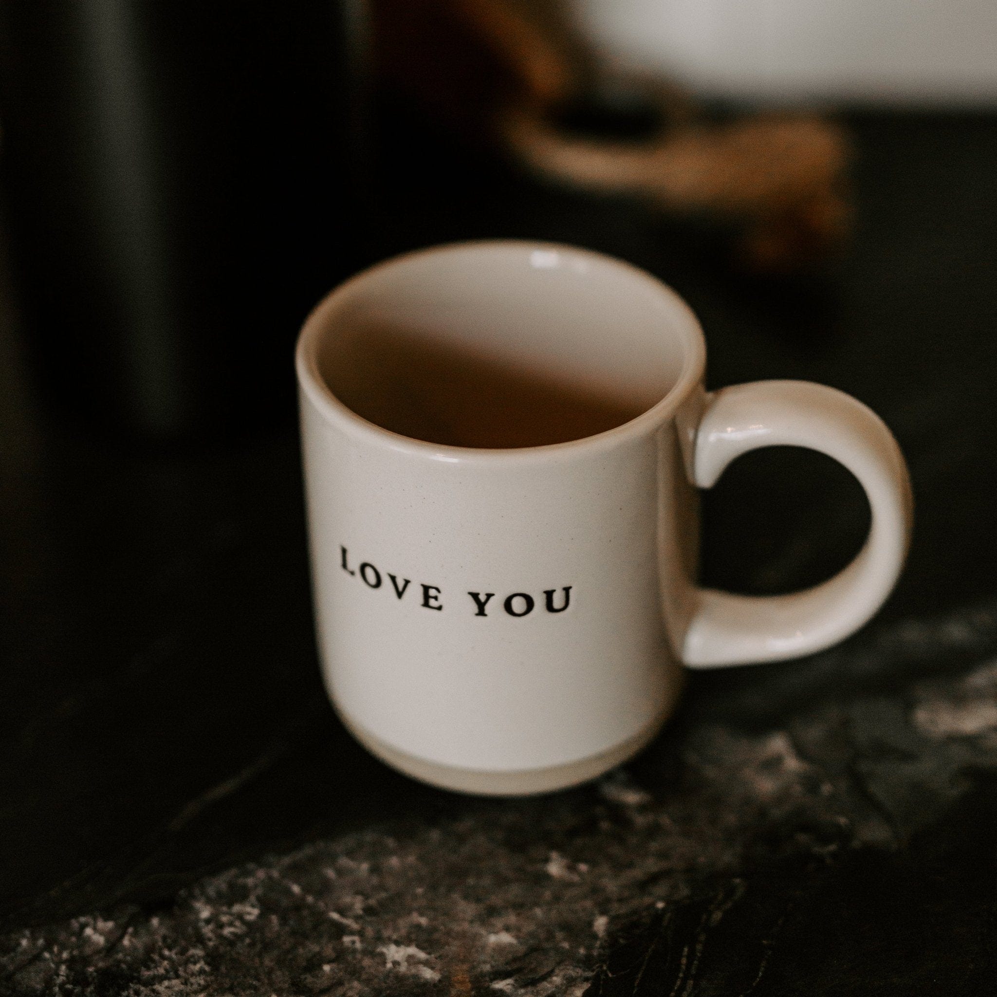 Cream stoneware mug with "LOVE YOU" text printed on the front, sitting on dark surface