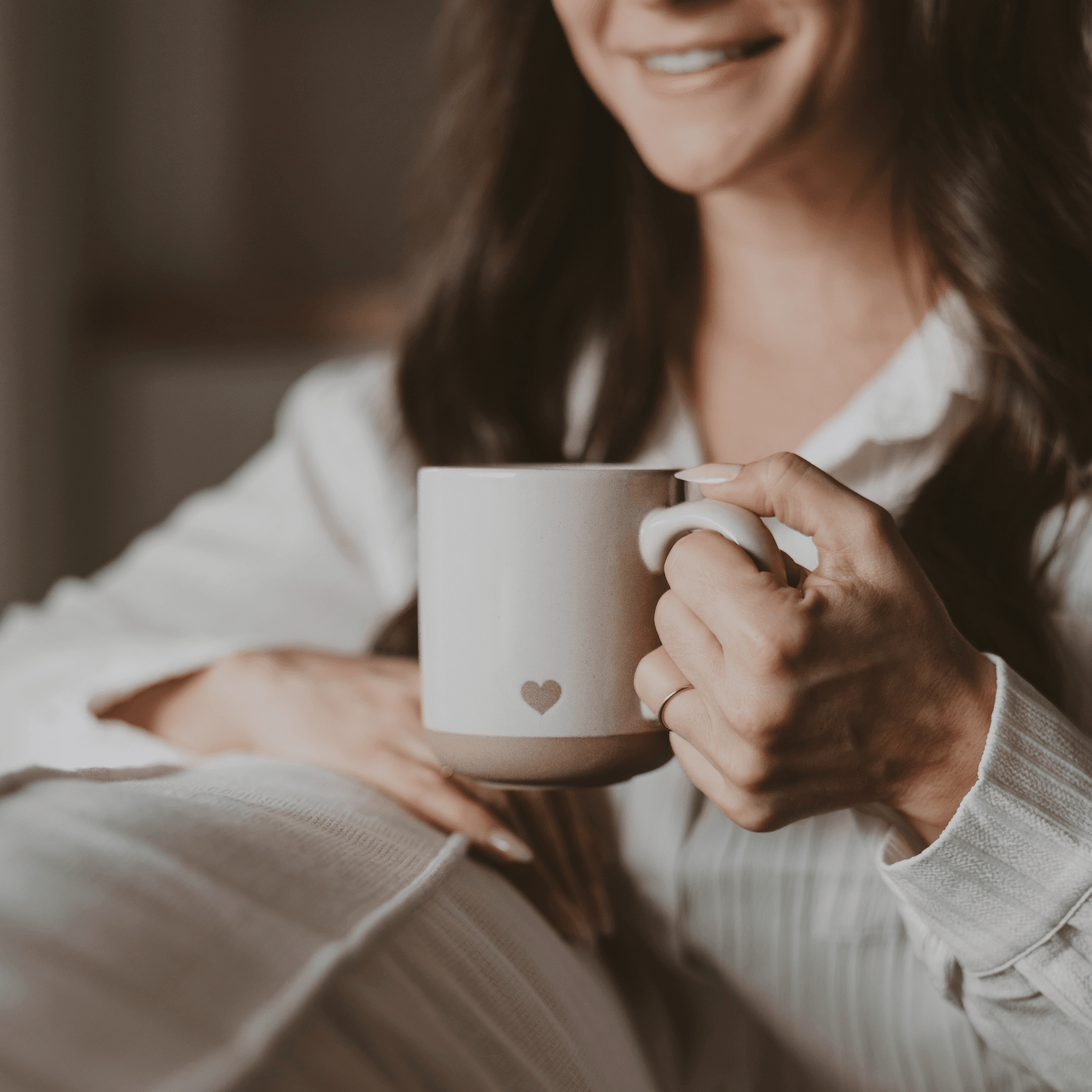 White stoneware mug with small heart design, held by couple's hands showing wedding rings