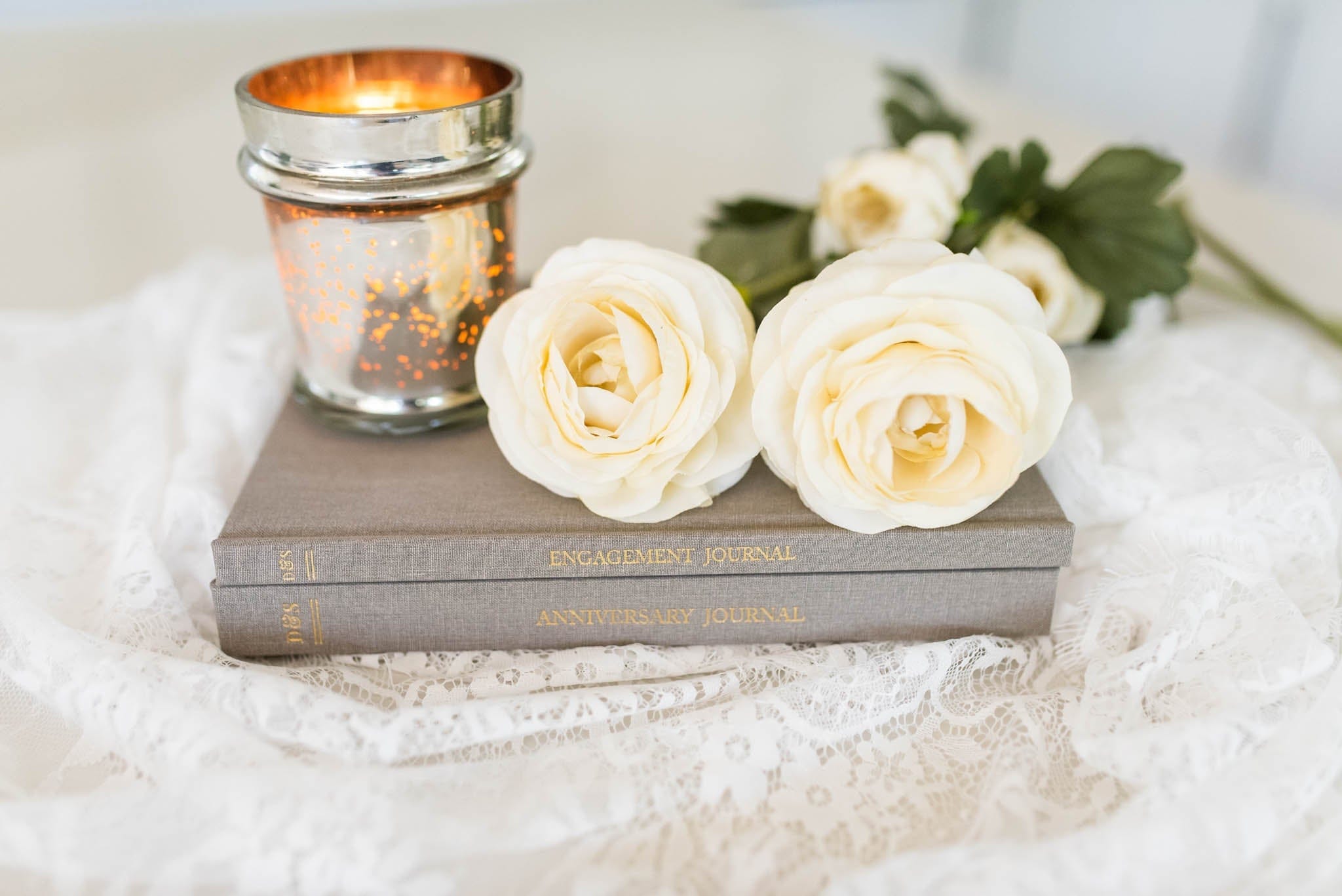 Gray leather anniversary journal displayed on lace with white roses and gold candle