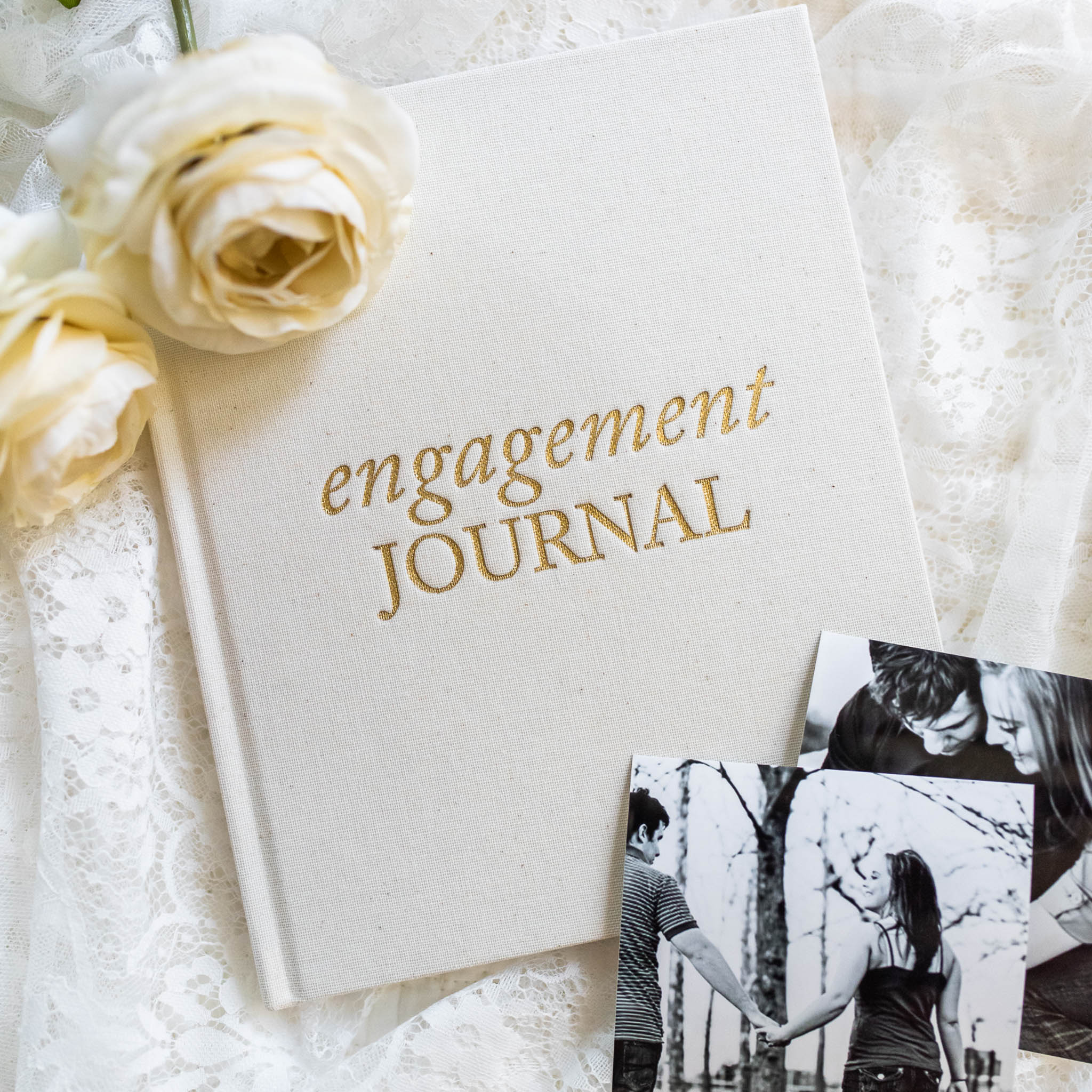 White hardcover engagement journal with gold foil text, styled with cream roses and black and white photos