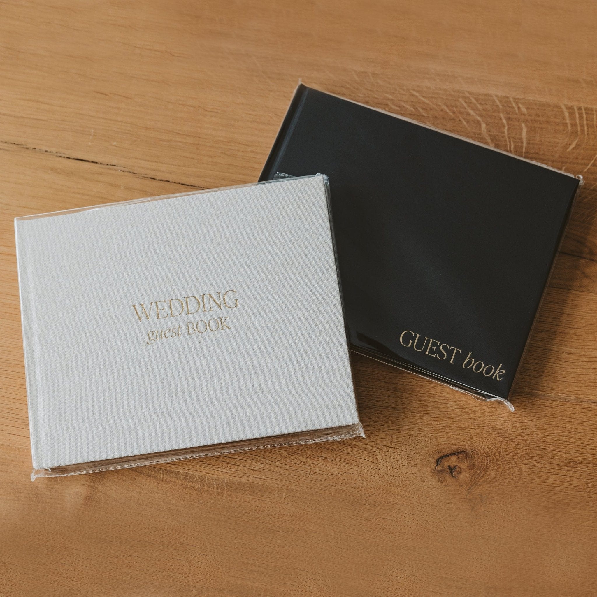 White and black wedding guest books with gold foil text on wooden surface