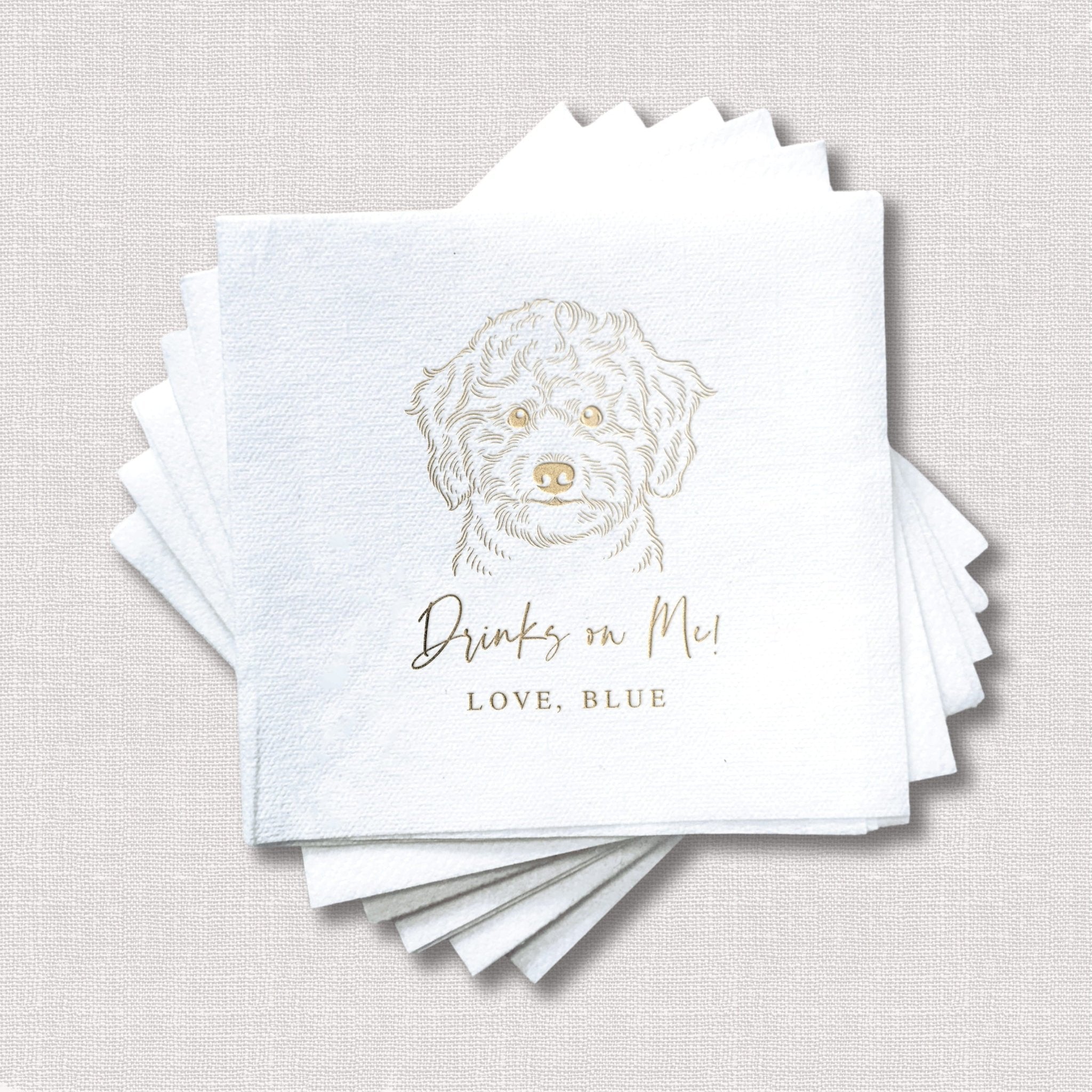 Stack of white napkins with gold foil-stamped dog portrait and "Drinks in Mud" text with "LOVE, BLUE" personalization below.