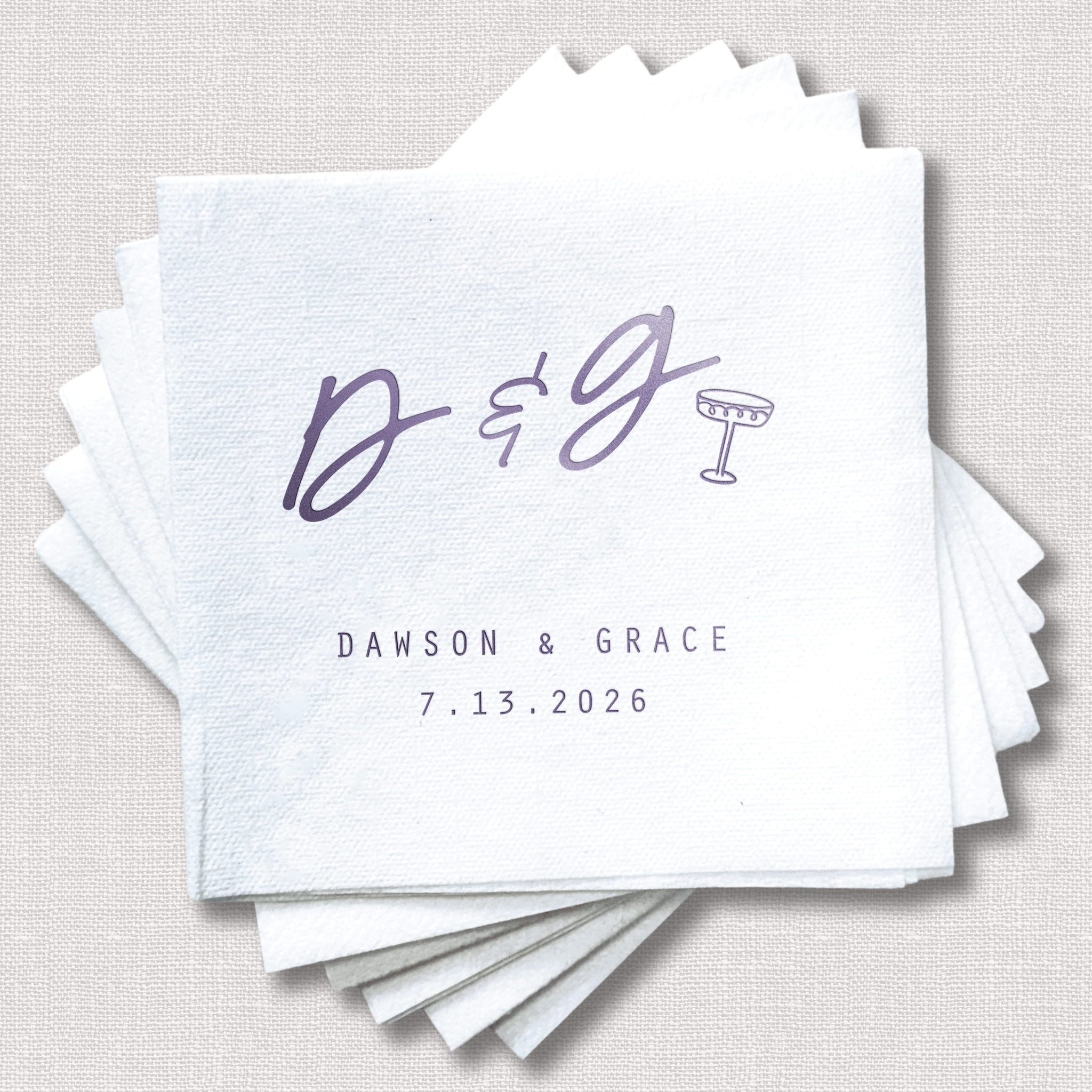 Stack of white cocktail napkins with purple foil-stamped design reading "D&G" with initials and "DAWSON & GRACE 7.13.2026"