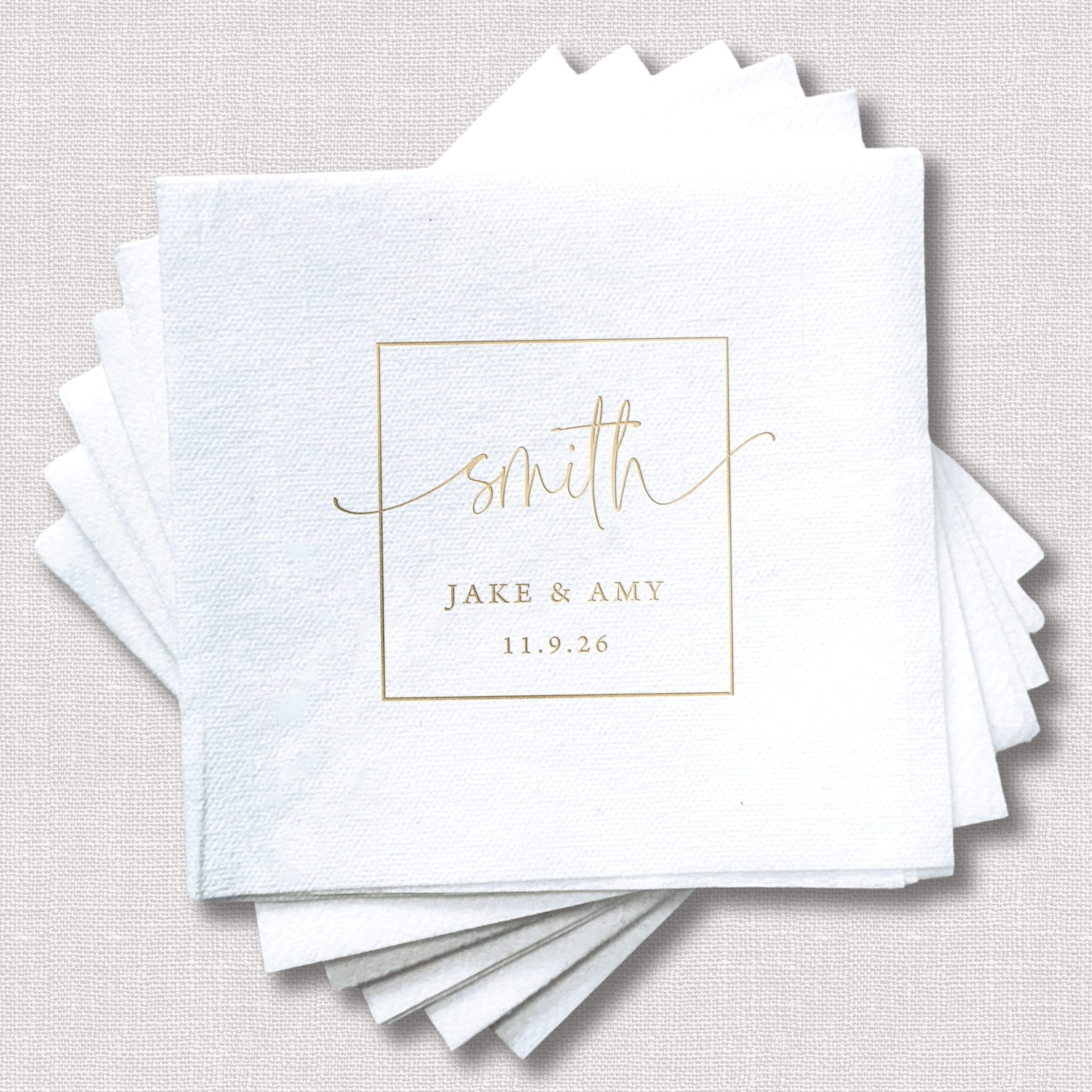 Stack of white linen napkins with gold foil-stamped monogram "smith" and names "Jake & Amy" with wedding date 11.9.28