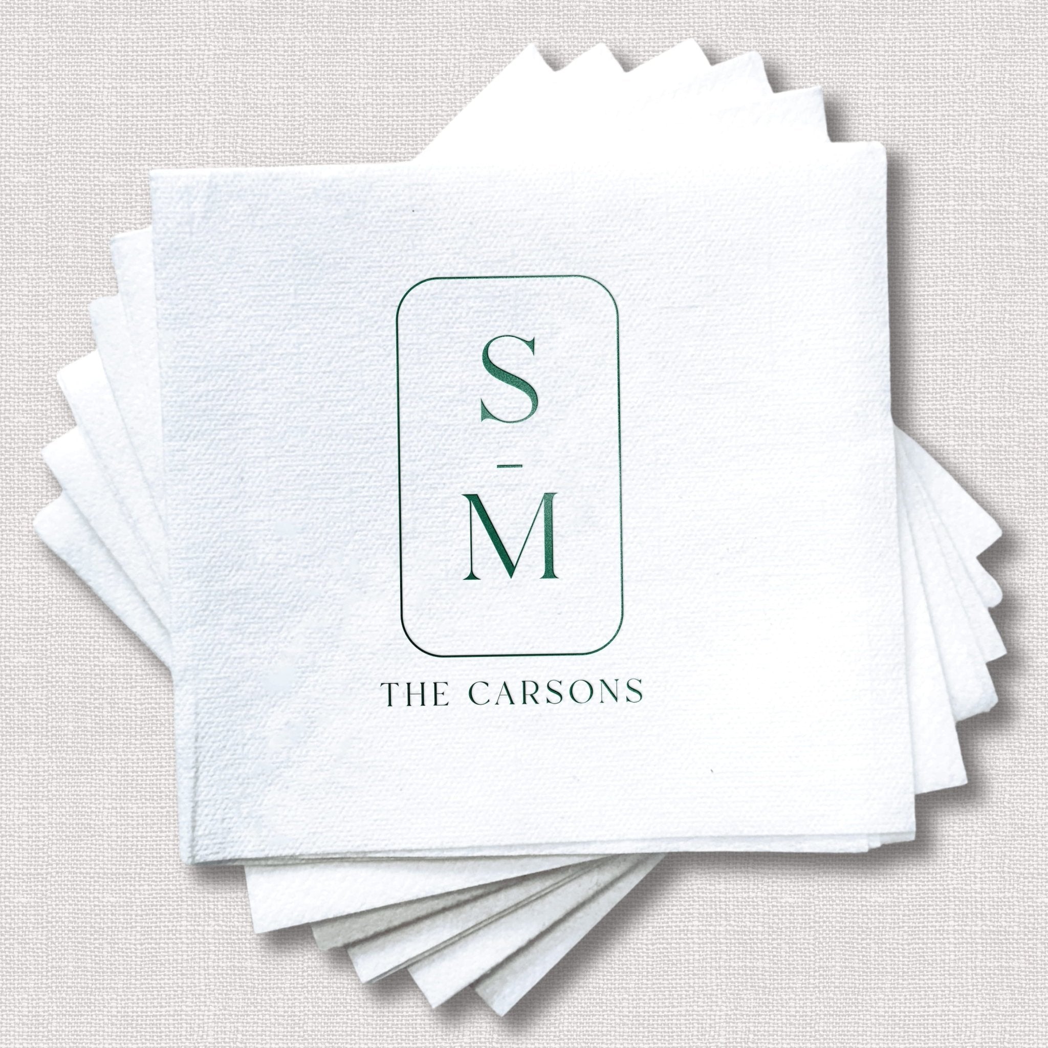 Stack of white linen napkins with green foil-stamped initials S and M and "The Carsons" text below