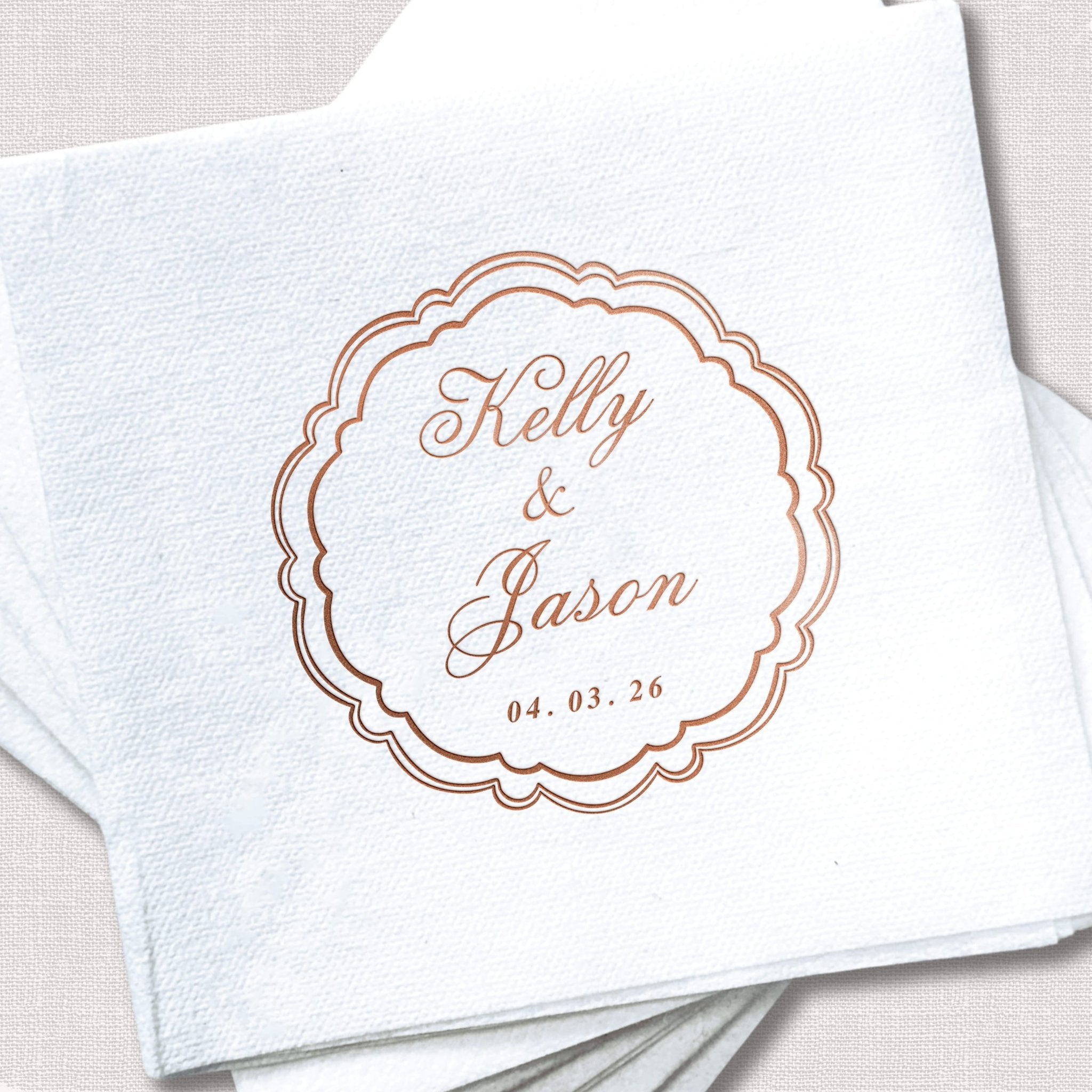 White cocktail napkin with rose gold scalloped frame design featuring "Kelly & Jason" and wedding date "04.03.28"