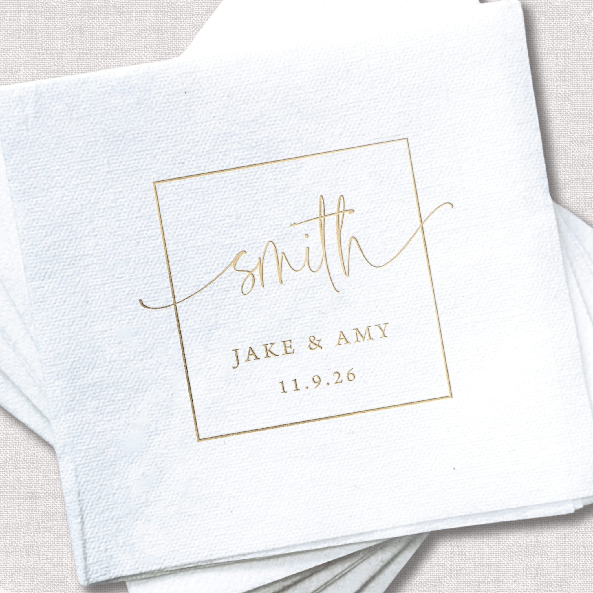 White linen napkin with gold foil monogram design reading "smith" with "Jake & Amy 11.9.26" underneath in a decorative frame