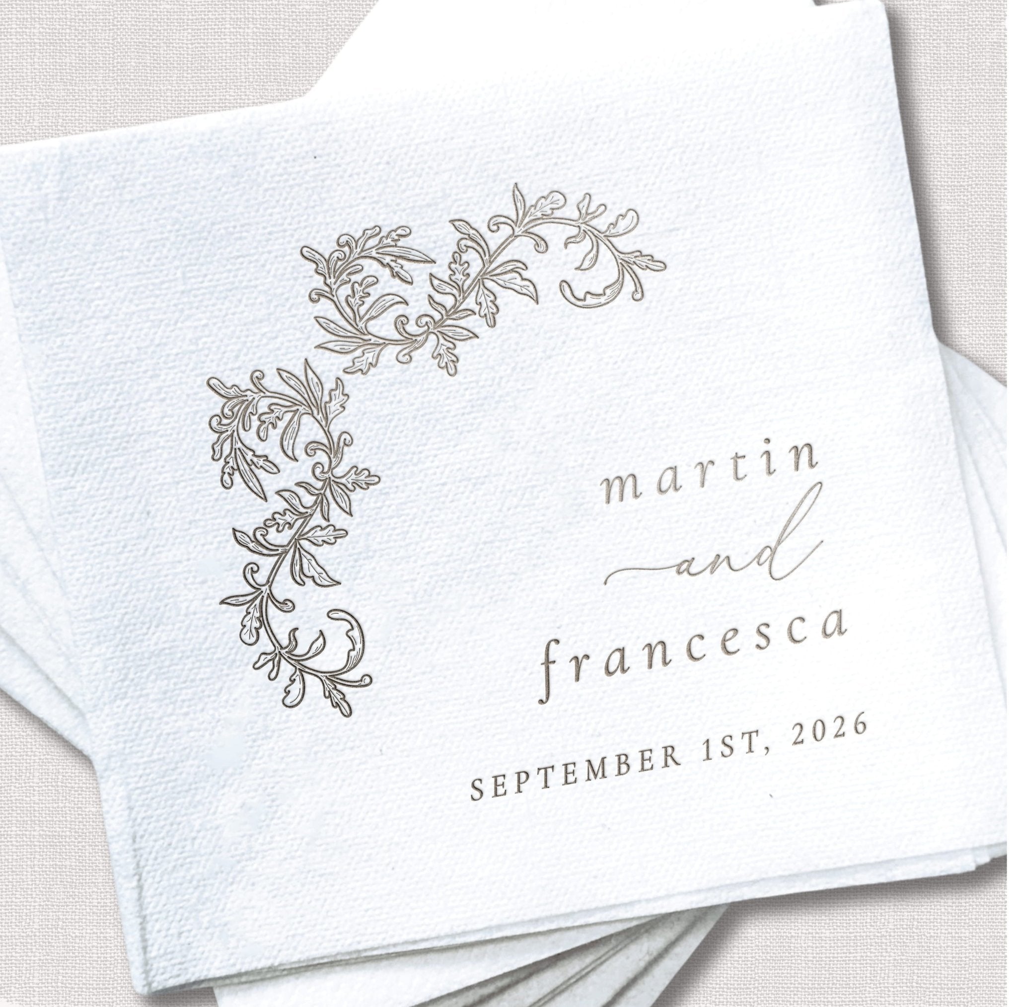 White linen cocktail napkin with ornate floral design and personalized text reading "martin and francesca" with "september 1st, 2026" date.