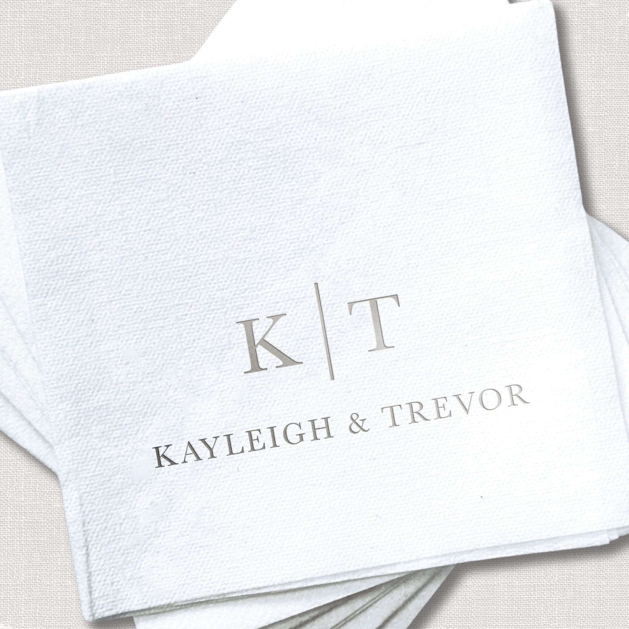 White linen napkins with silver foil-stamped initials K T and names Kayleigh & Trevor stacked together