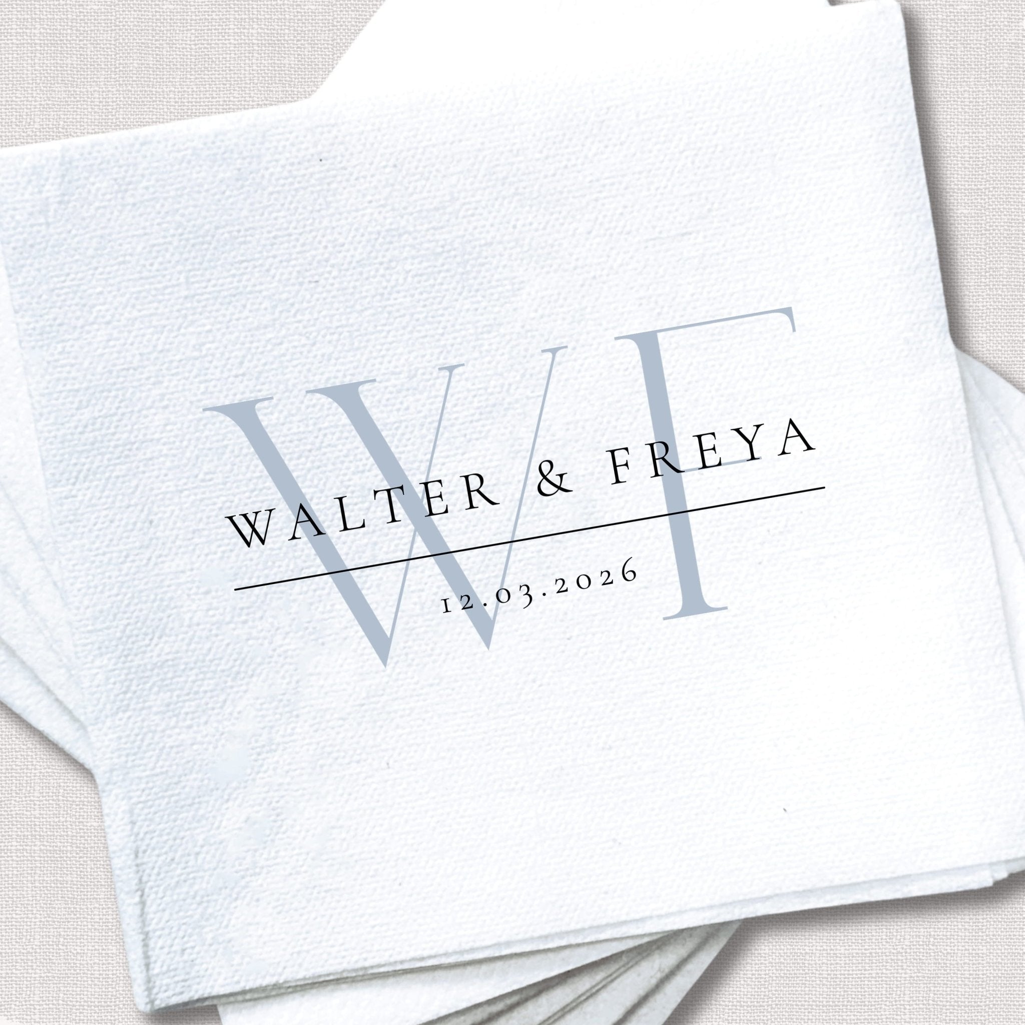 White cocktail napkin with personalized initials "W" and "F" and wedding details "WALTER & FREYA" with date "14.03.2026"