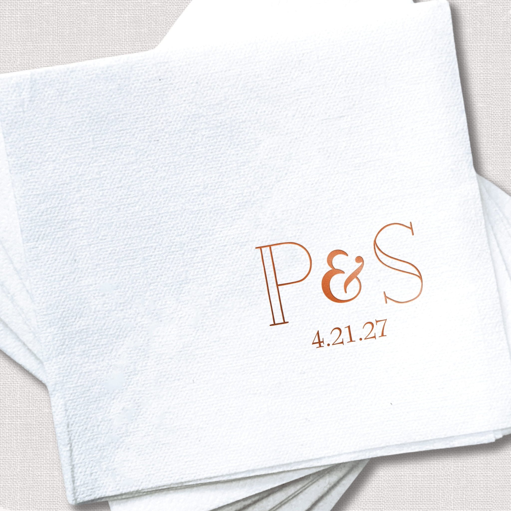 White linen napkin with rose gold foil-stamped initials P&S and wedding date 4.21.27