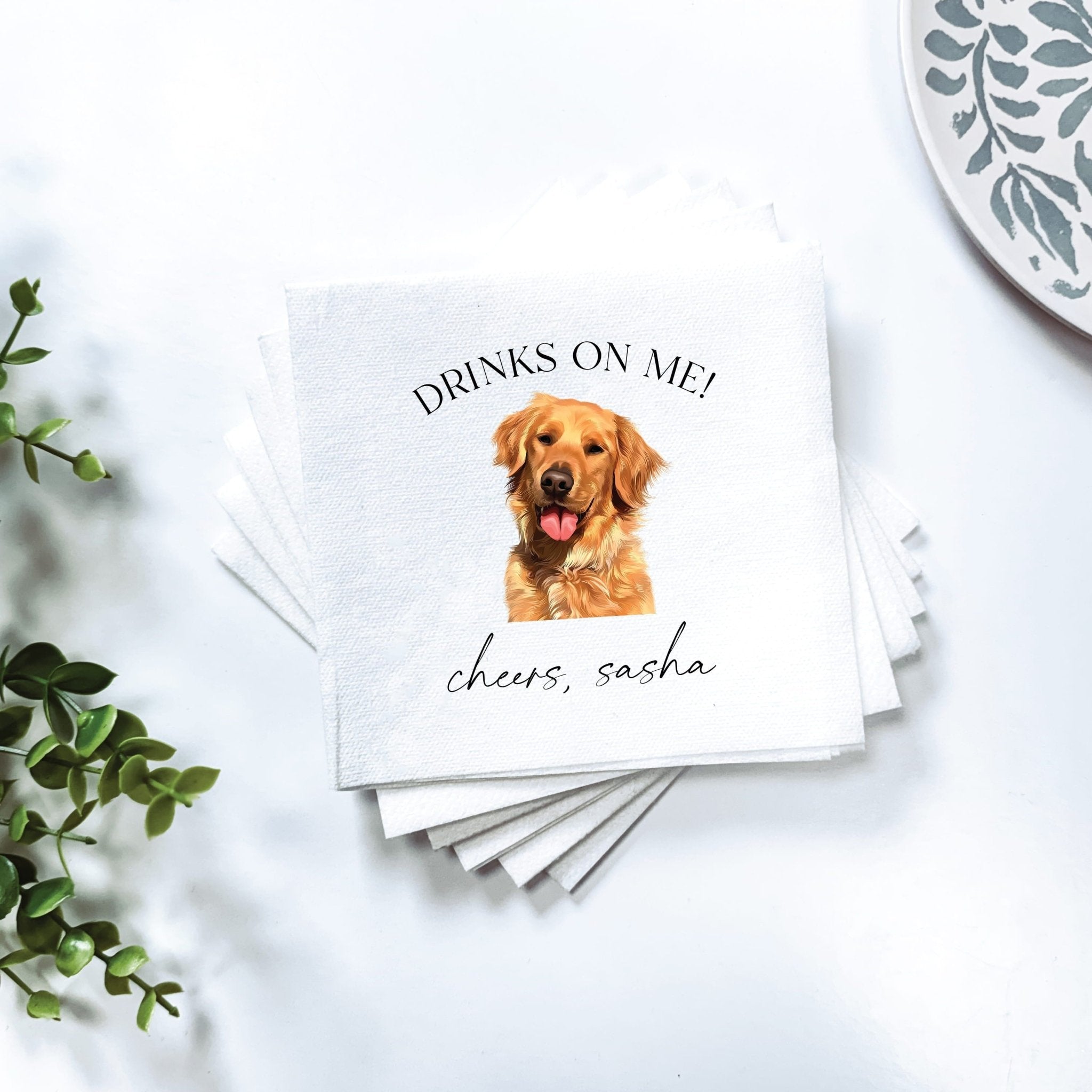 Stack of white napkins with golden retriever and "Drinks on Me" text, personalized with name "Sasha" below dog image