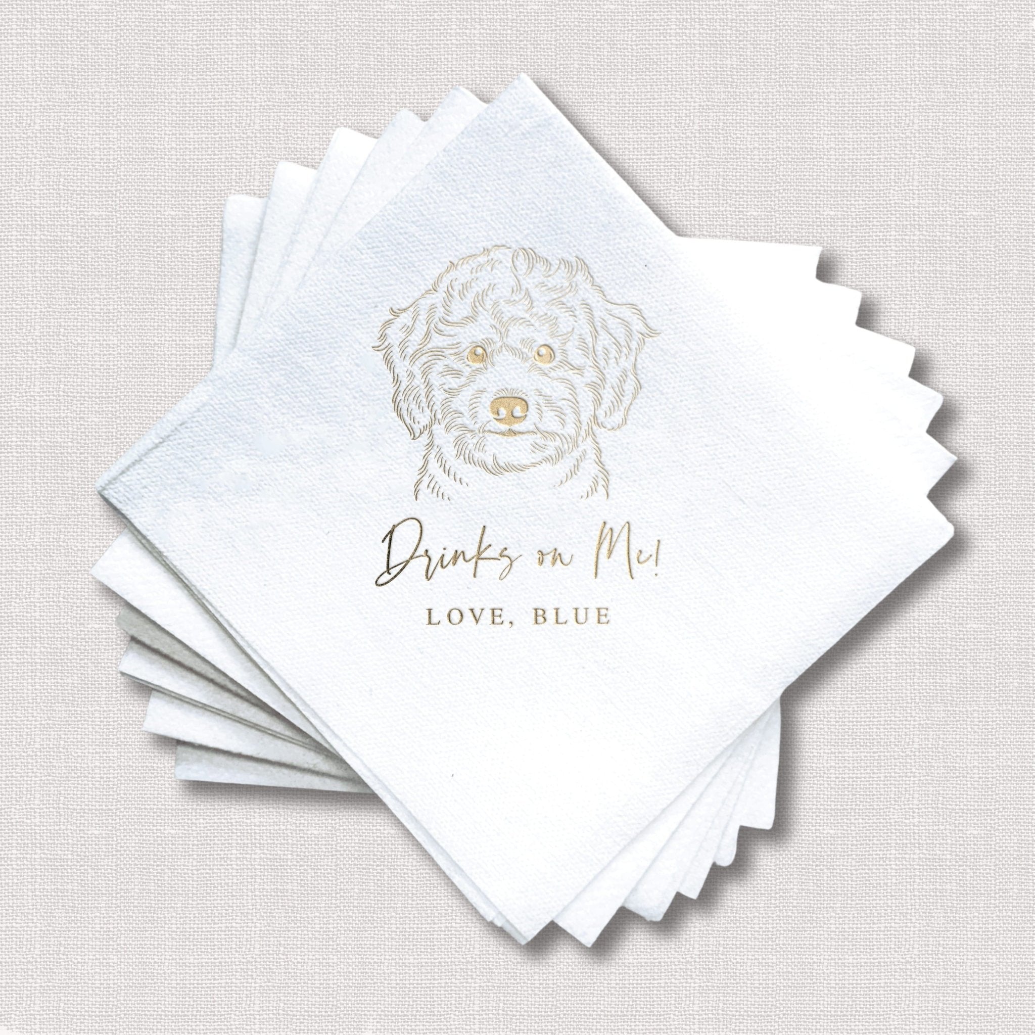 Stack of white linen napkins with gold foil stamped dog illustration and "Drinks on Me" text personalized with "LOVE, BLUE"