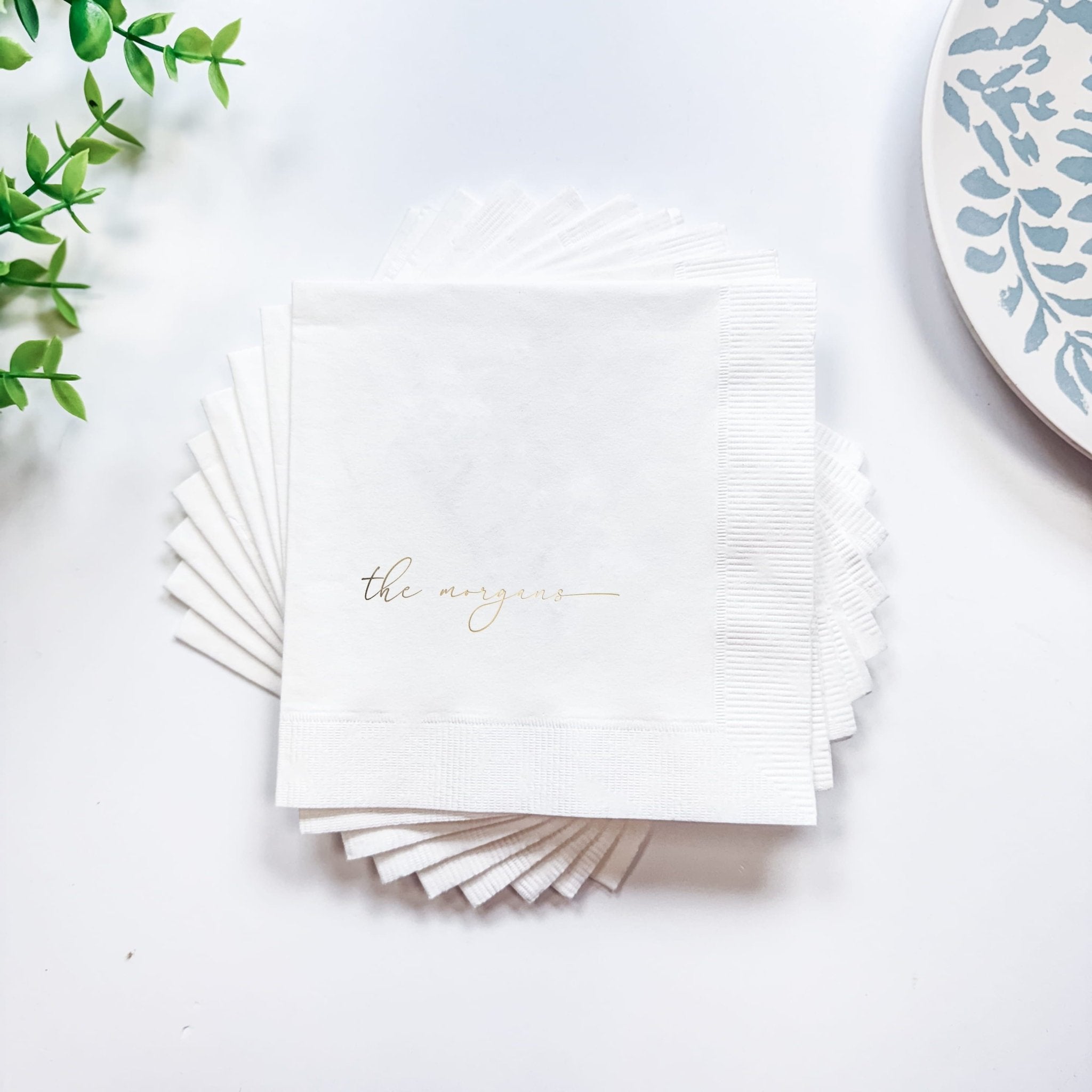 Stack of white foil-stamped cocktail napkins with "the newlyweds" text in gold lettering