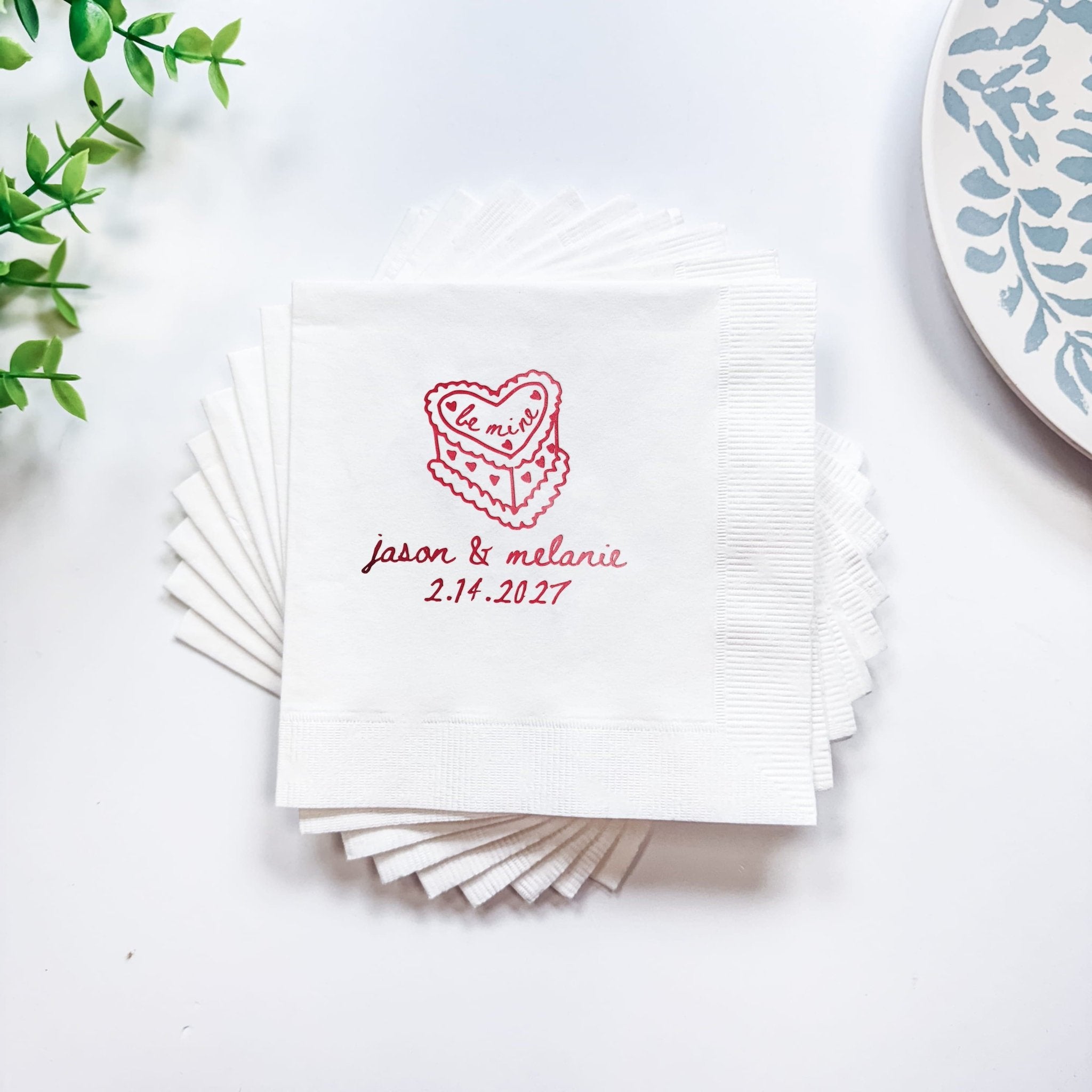 Stack of white napkins with red foil-stamped layered heart design and personalized names and date