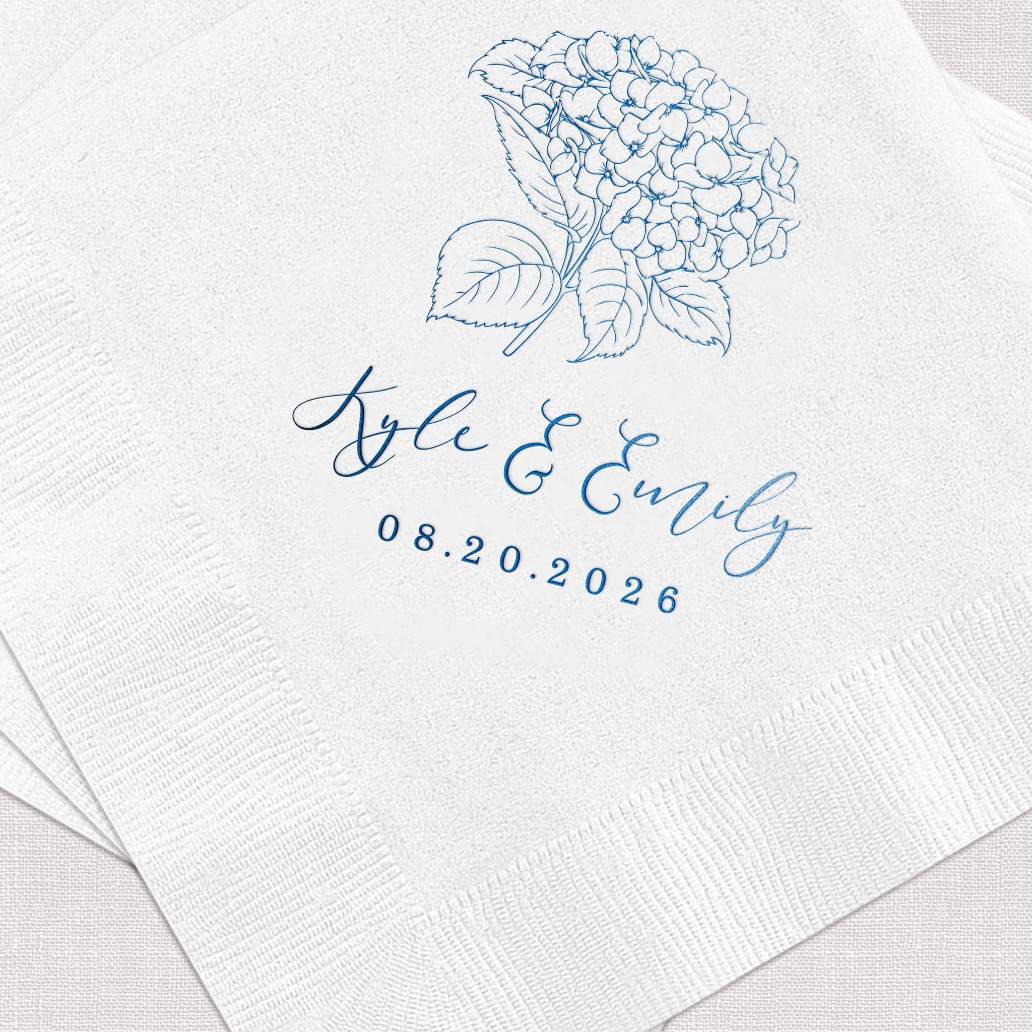 White napkin with blue foil-stamped hydrangea design, couple's names and wedding date 08.20.2026