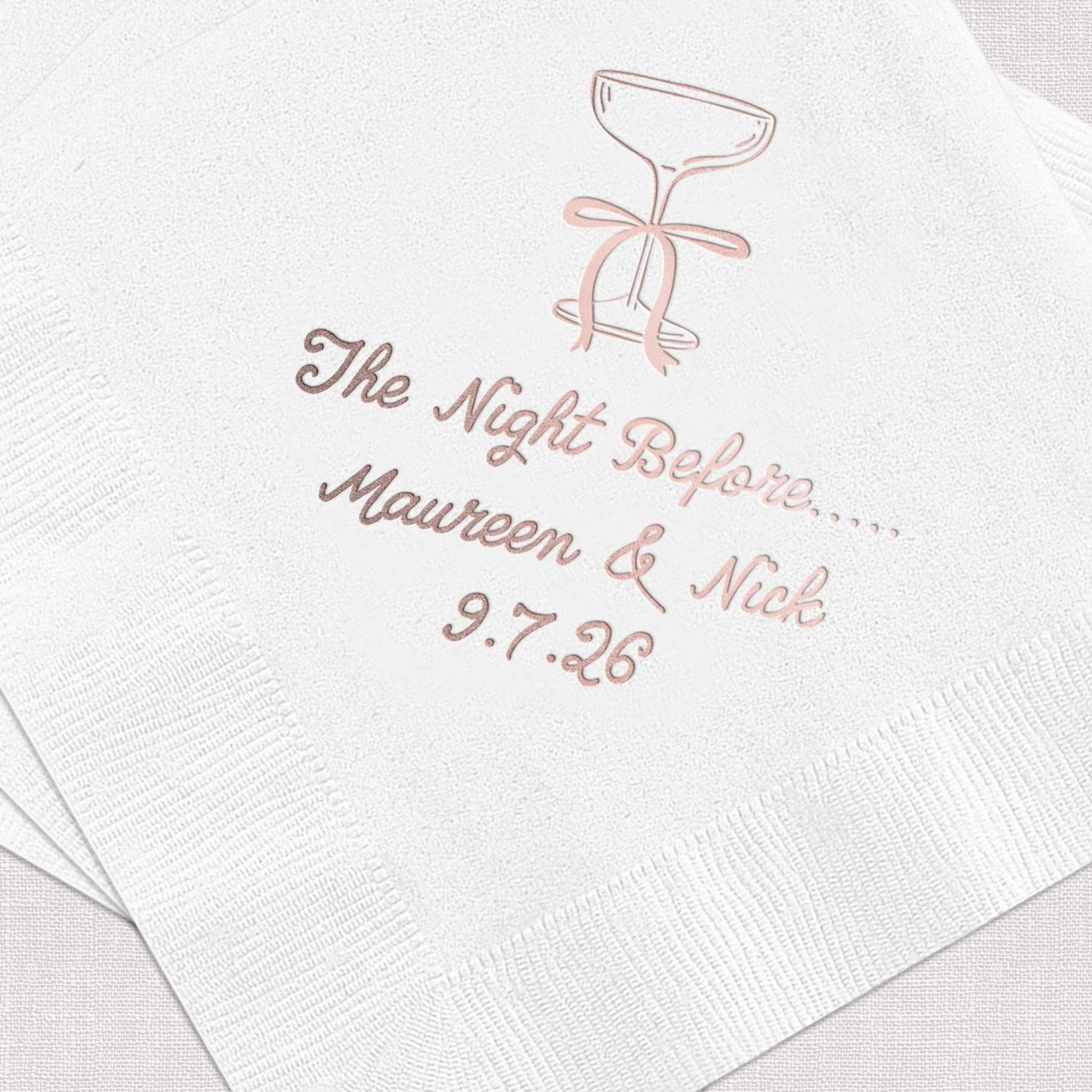 White cocktail napkins with rose gold foil-stamped martini glass and personalized text reading "The Night Before Maureen & Nick 9.7.26"
