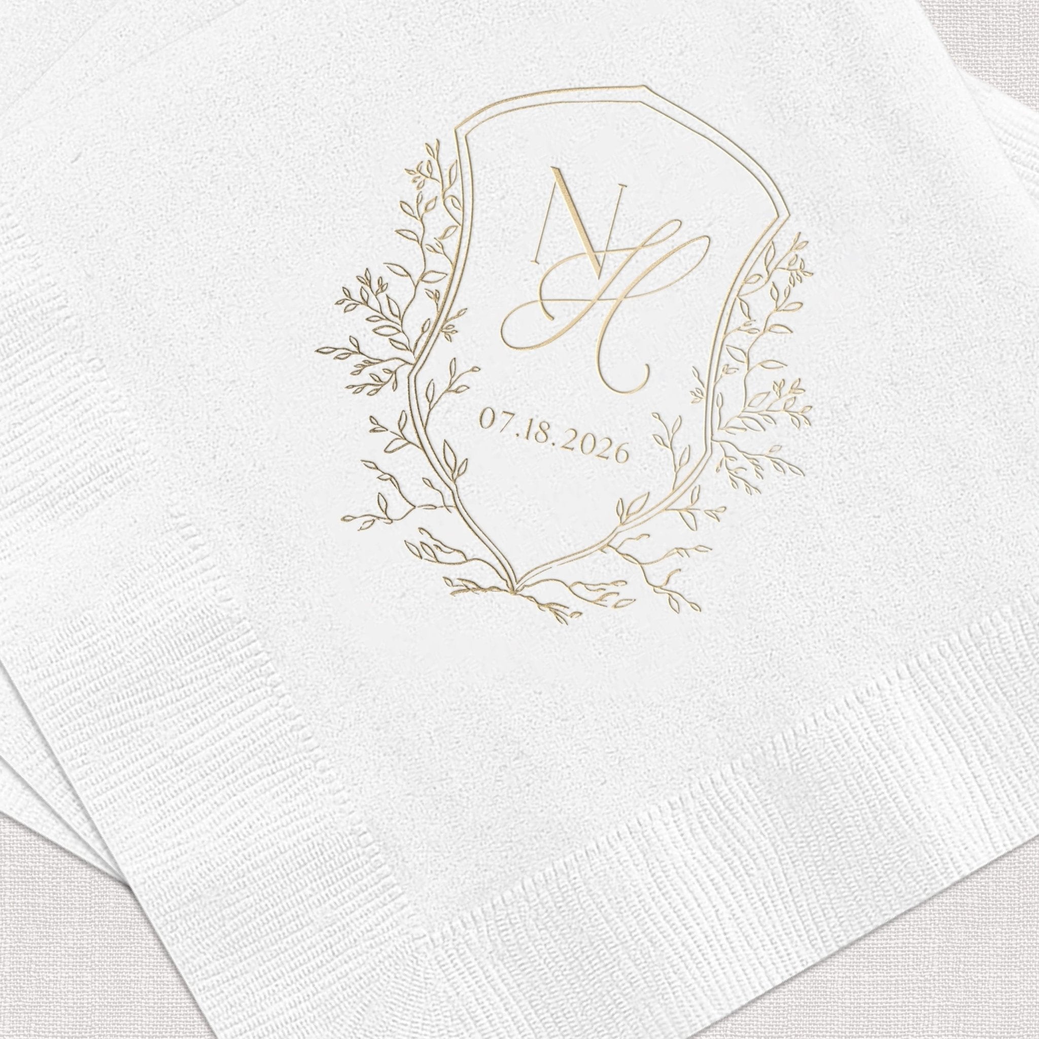 White napkin with gold foil botanical wreath monogram and wedding date 07.18.2026