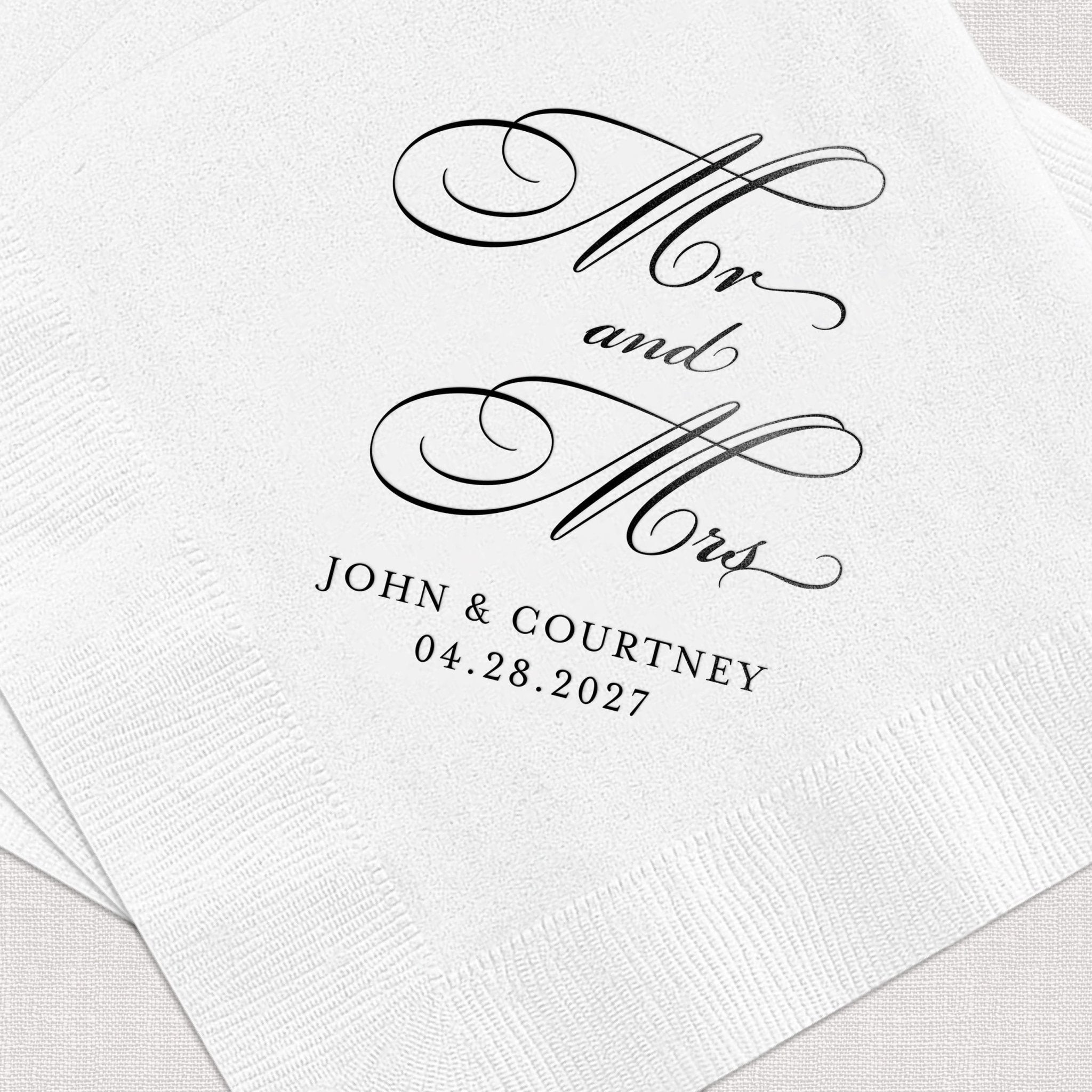 White napkin with elegant black script reading "Mr and Mrs," ornate flourishes, and "JOHN & COURTNEY 04.28.2027" personalization.