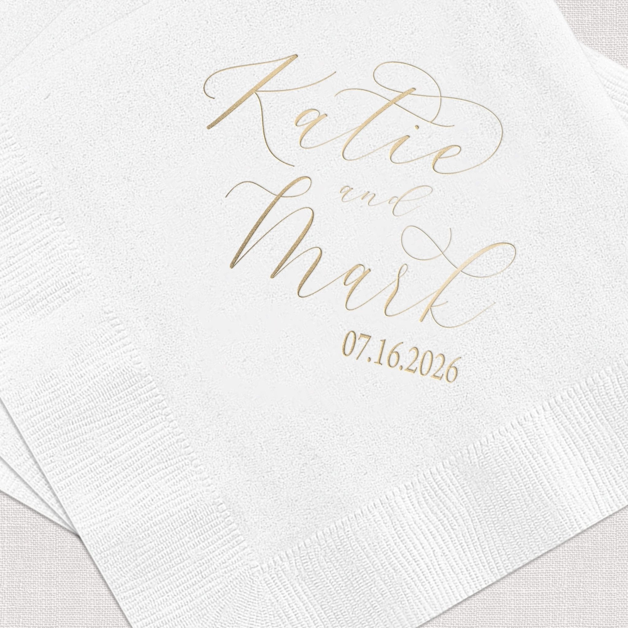 White beverage napkin with gold foil stamped text reading "Kate on Mark" and wedding date 07.16.2026.