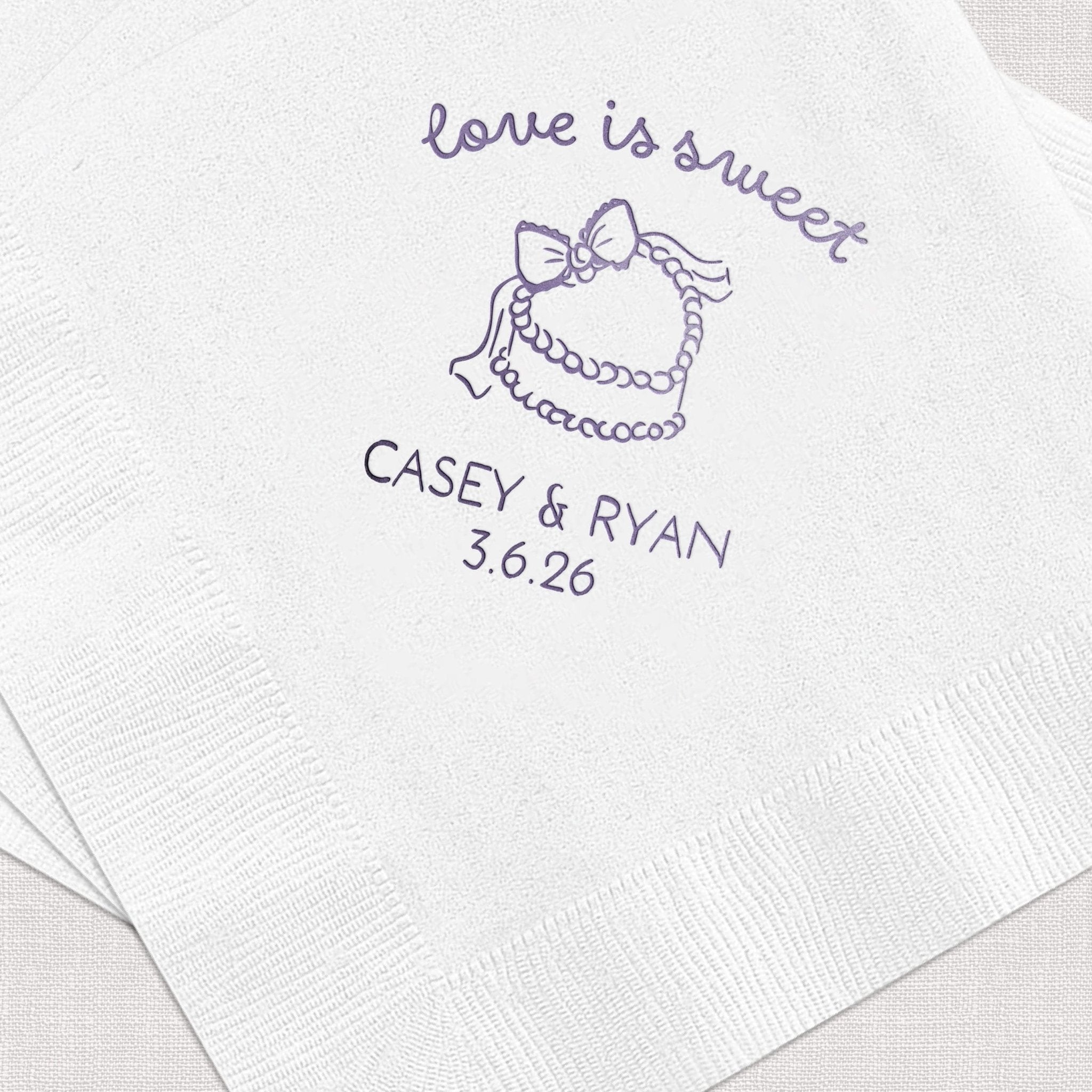 White cocktail napkins with purple foil-stamped design featuring "love is sweet" text, tiered cake illustration, and "CASEY & RYAN 3.6.26" personalization.