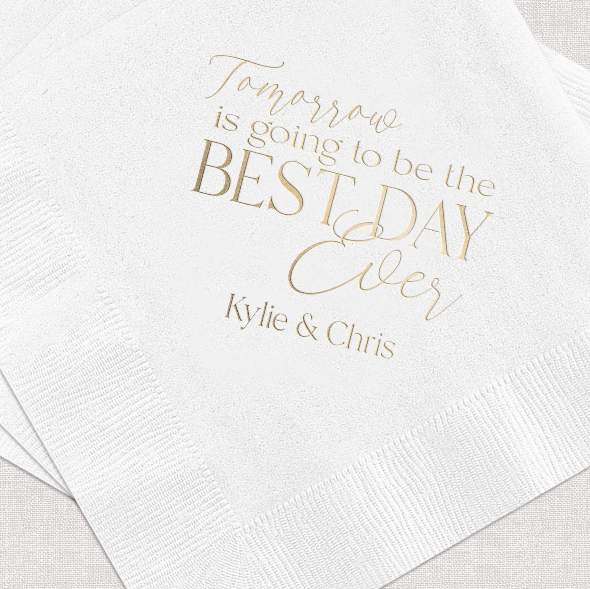 White cocktail napkins with gold foil text reading "Tomorrow is going to be the BEST DAY ever" and personalized names Kylie & Chris