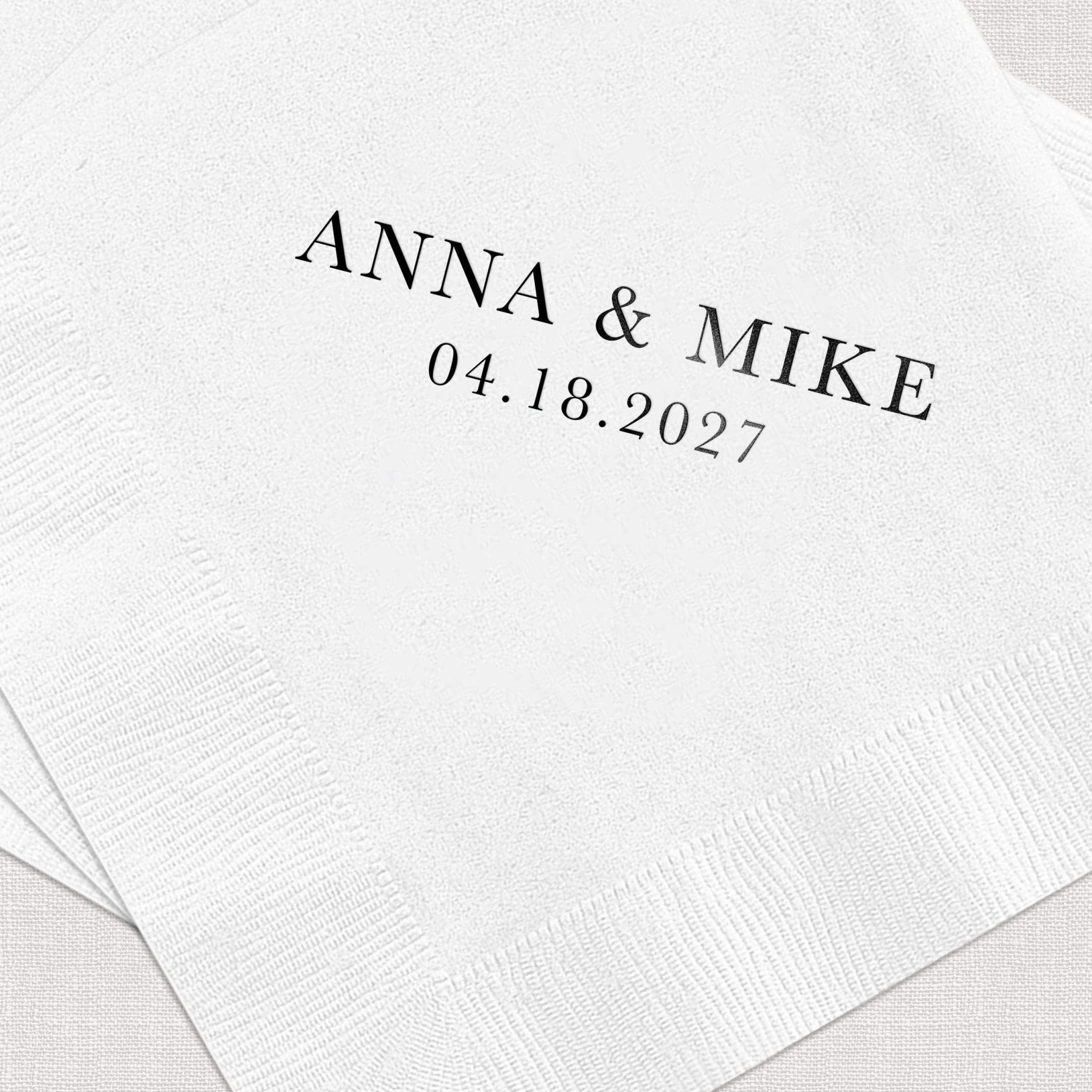 White cocktail napkins with "ANNA & MIKE 04.18.2027" printed in black text