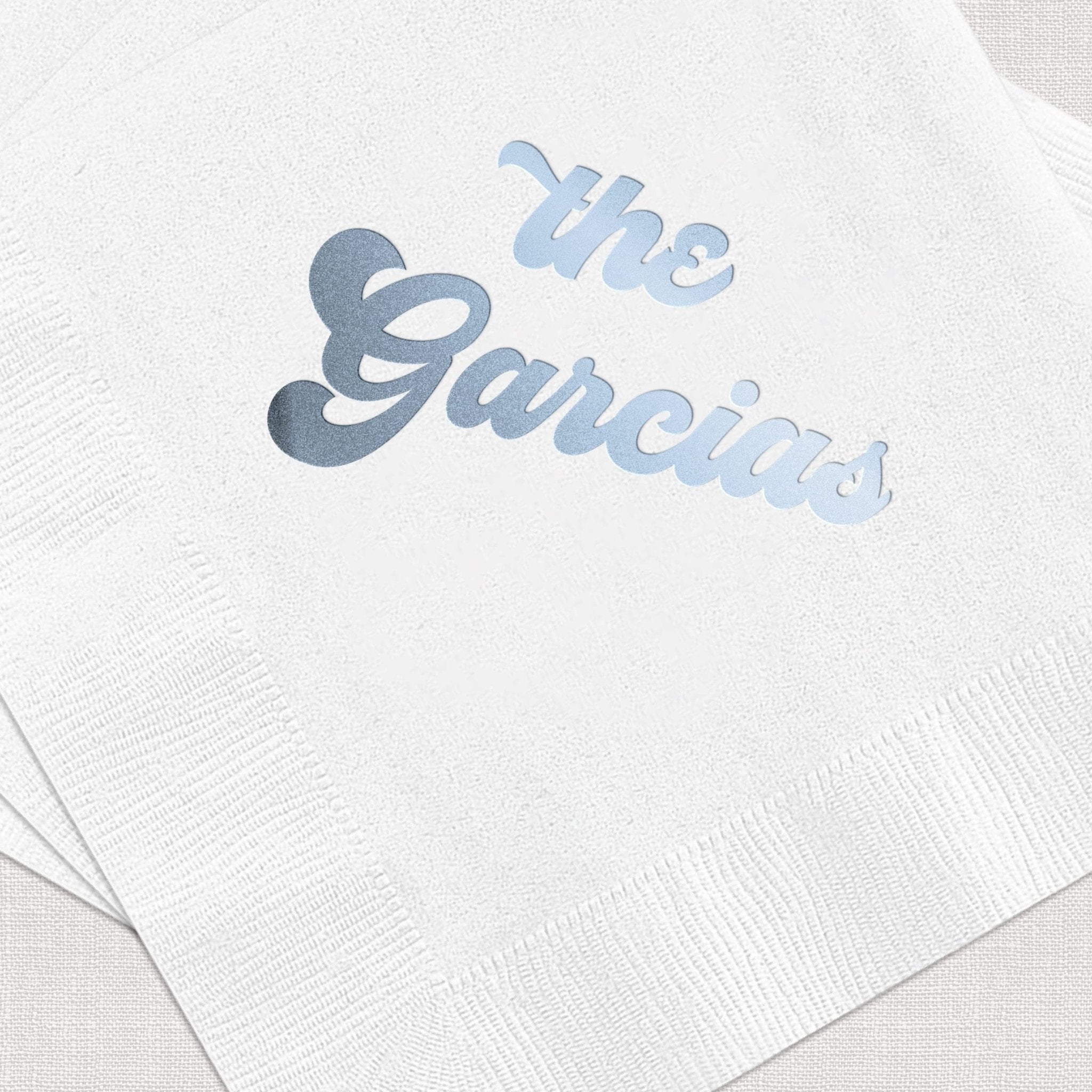 White cocktail napkin with blue foil stamped text reading "the Garcias"