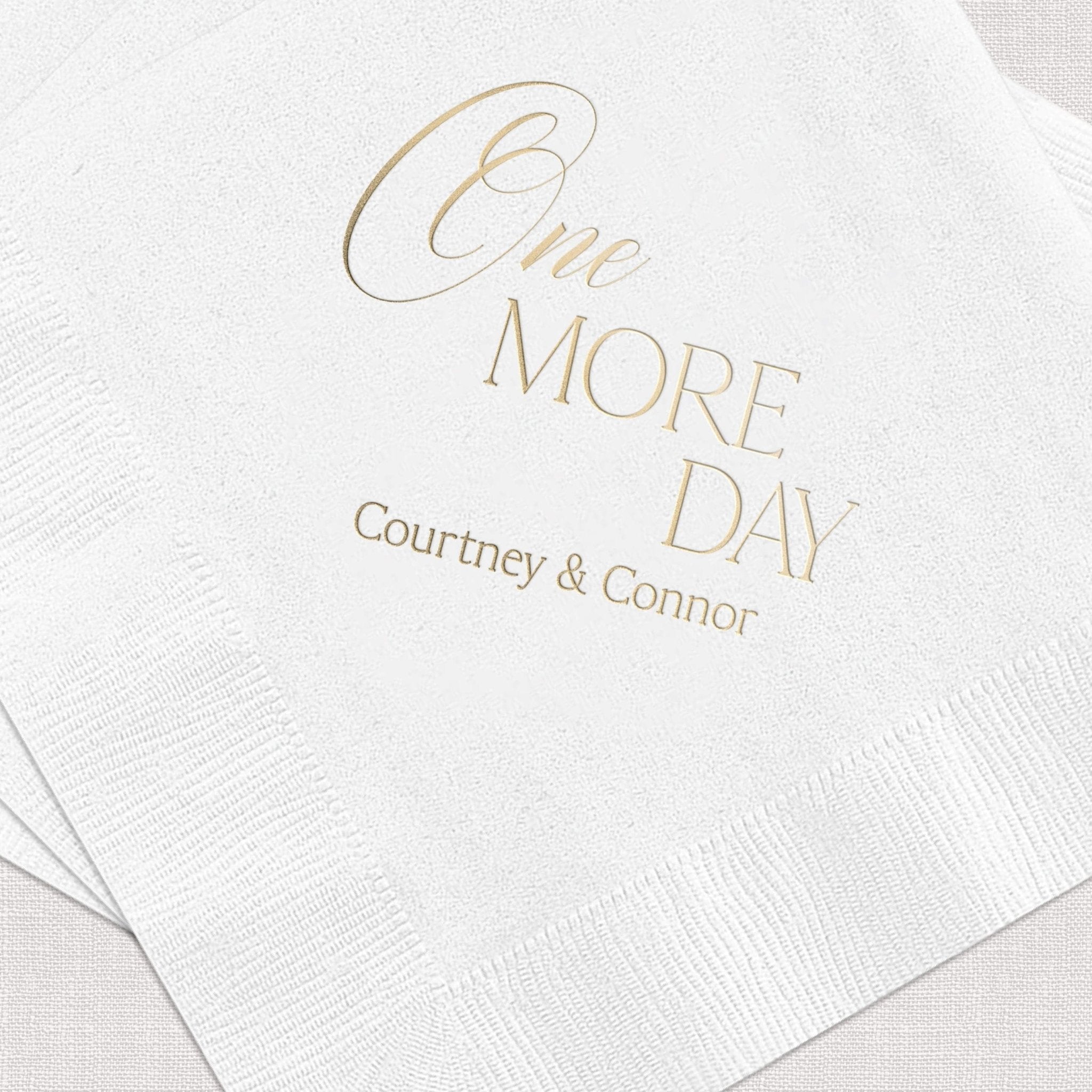 White cocktail napkins with gold foil stamped text reading "One MORE DAY" and personalized names "Courtney & Connor" below