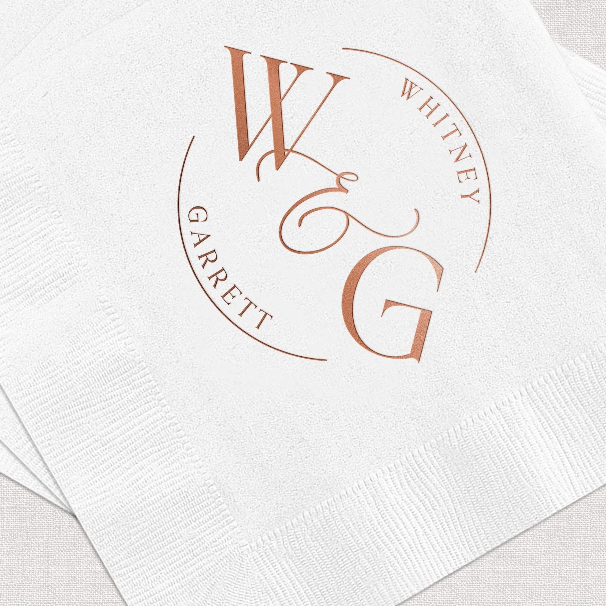 White cocktail napkins with rose gold foil circular monogram featuring initials W, G, and E with names Garrett and Whitney.