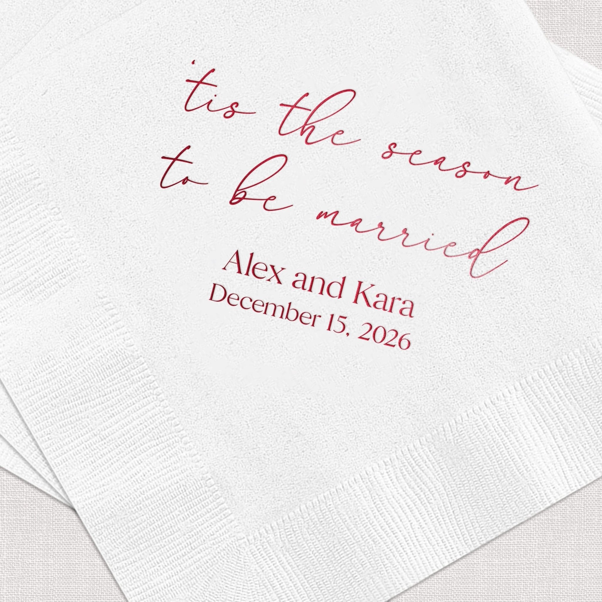 White napkin with burgundy foil-stamped text reading "tis the season to be married" and personalized names "Alex and Kara" with wedding date December 15, 2026.